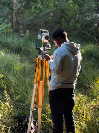Surveyor using a total station in a grassy field.