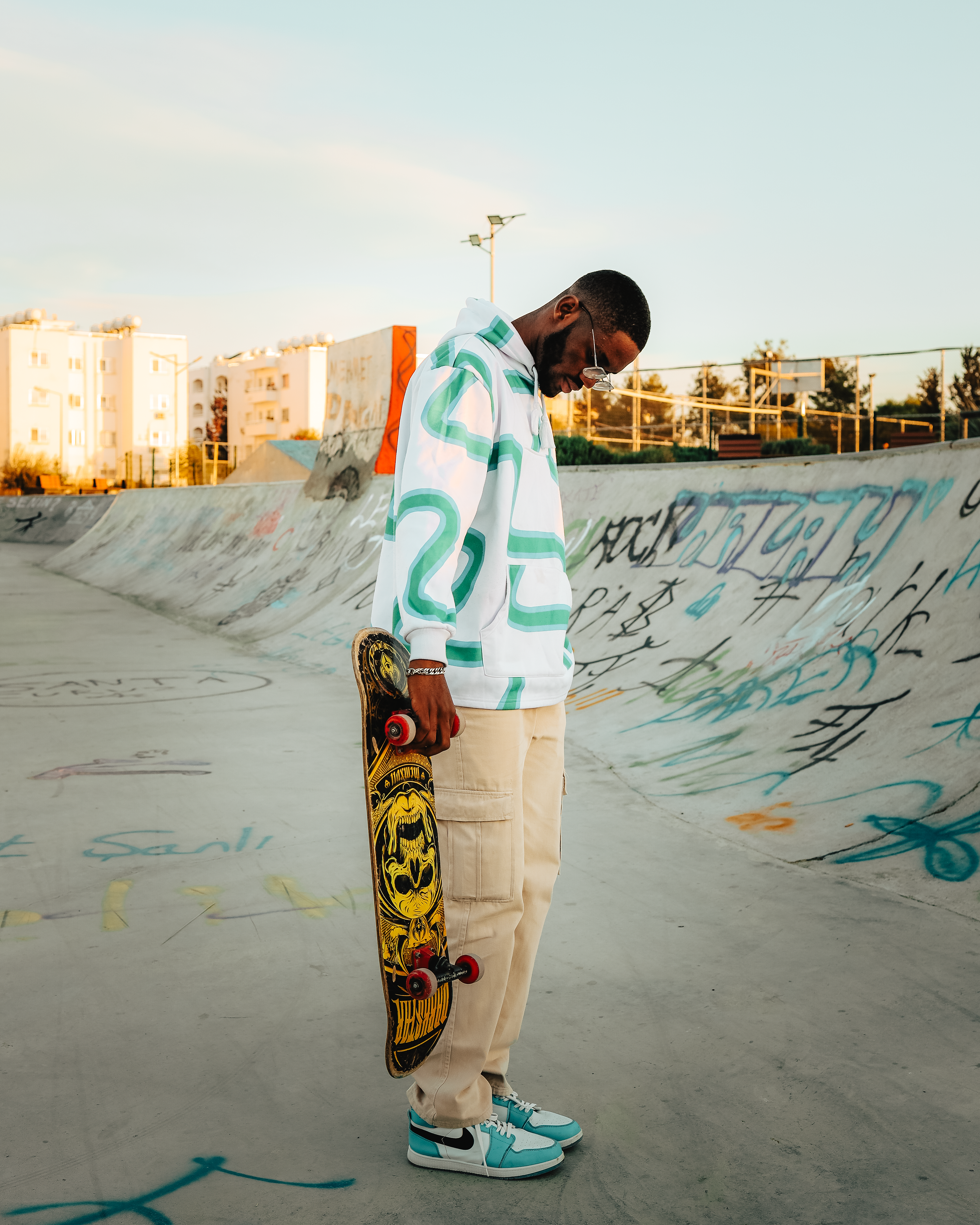 Man holding skateboard at skatepark during golden hour