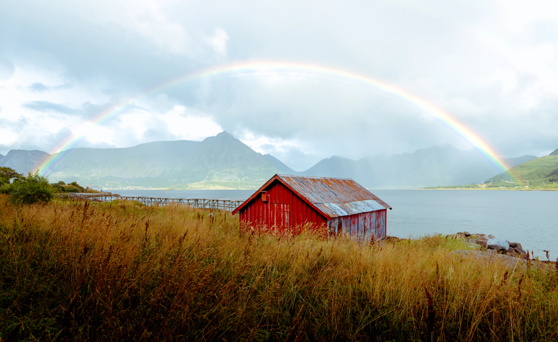 Red barn by lake with rainbow and mountains