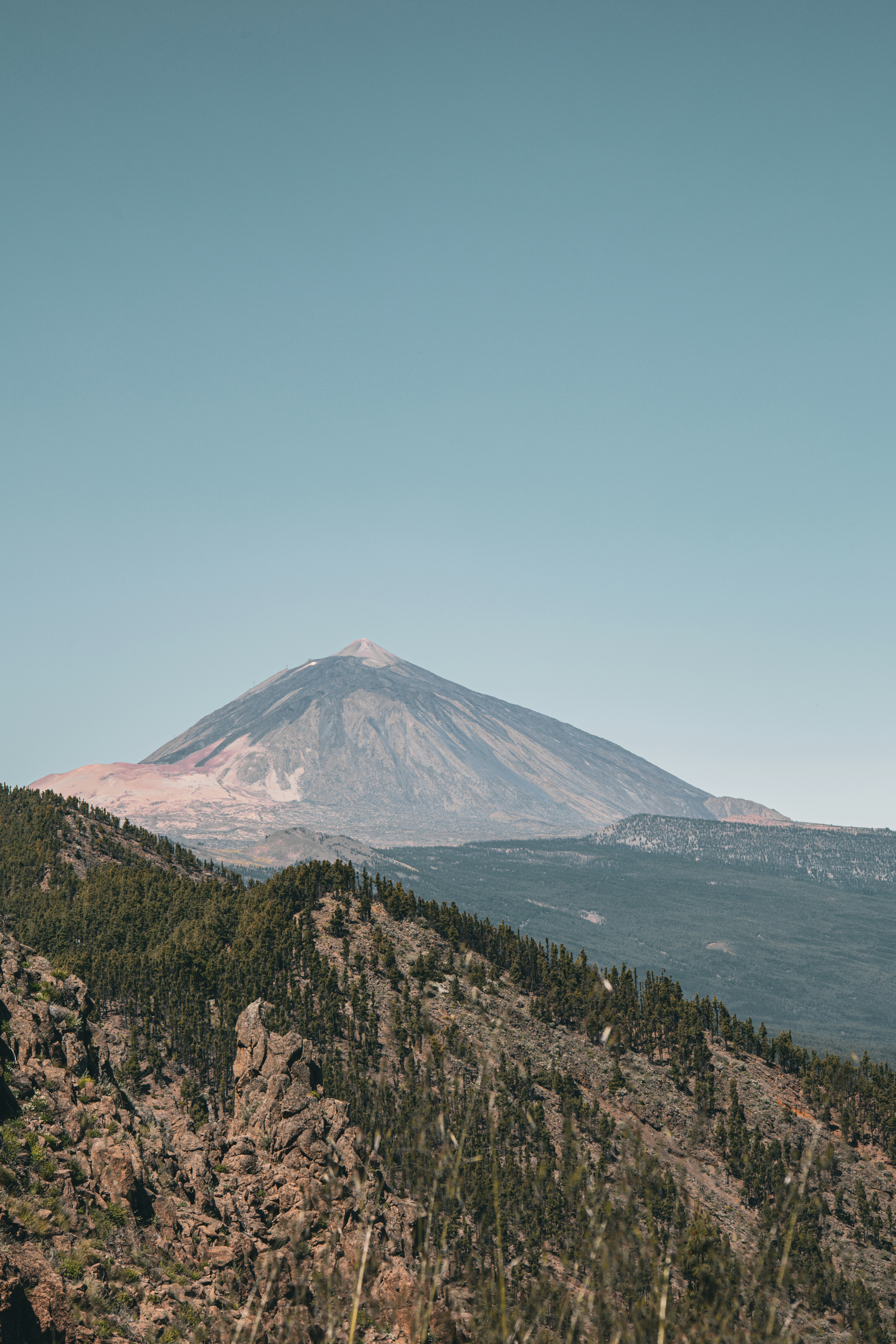La cima del vulcano si erge sopra montagne boscose sotto un cielo limpido