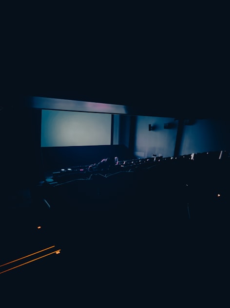 Empty movie theater with rows of seats facing a glowing lit screen in a dark auditorium