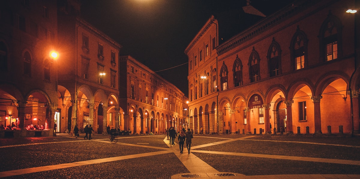 Bologna June — arched portico buildings lining a cobblestone square on a summer evening