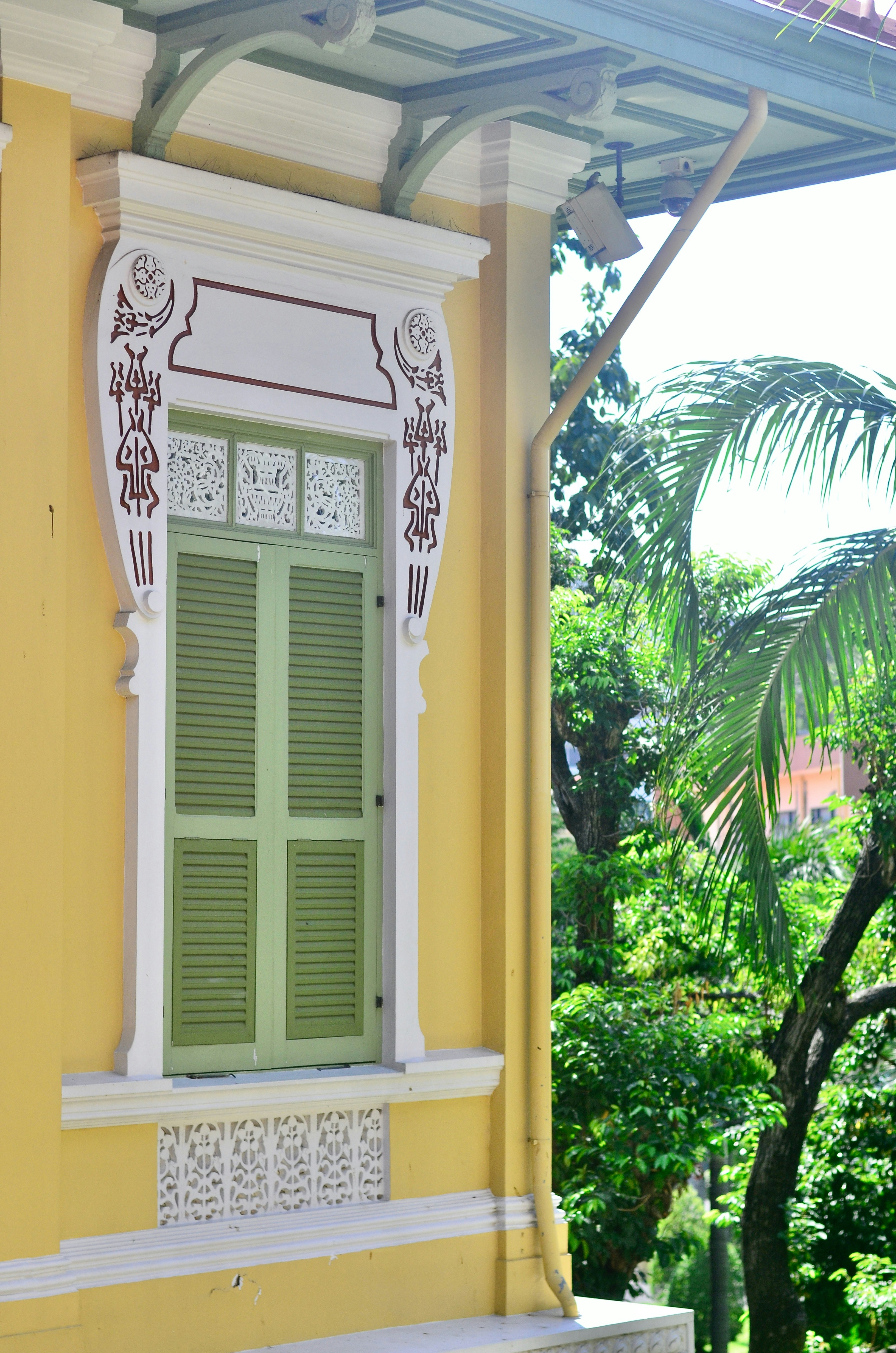 Yellow building with green shutters and palm trees.