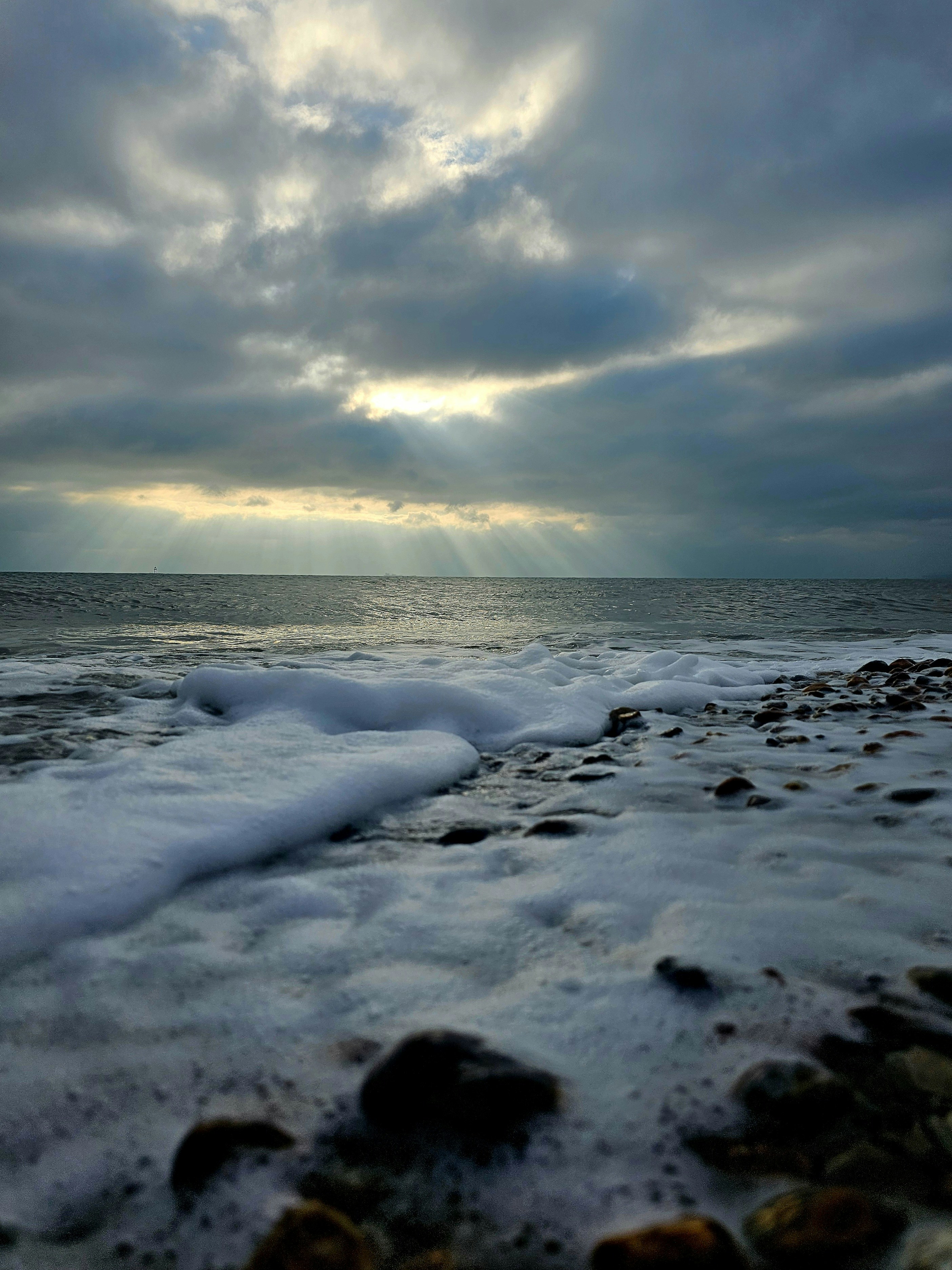 Sunbeams break through clouds over a foamy ocean shore.