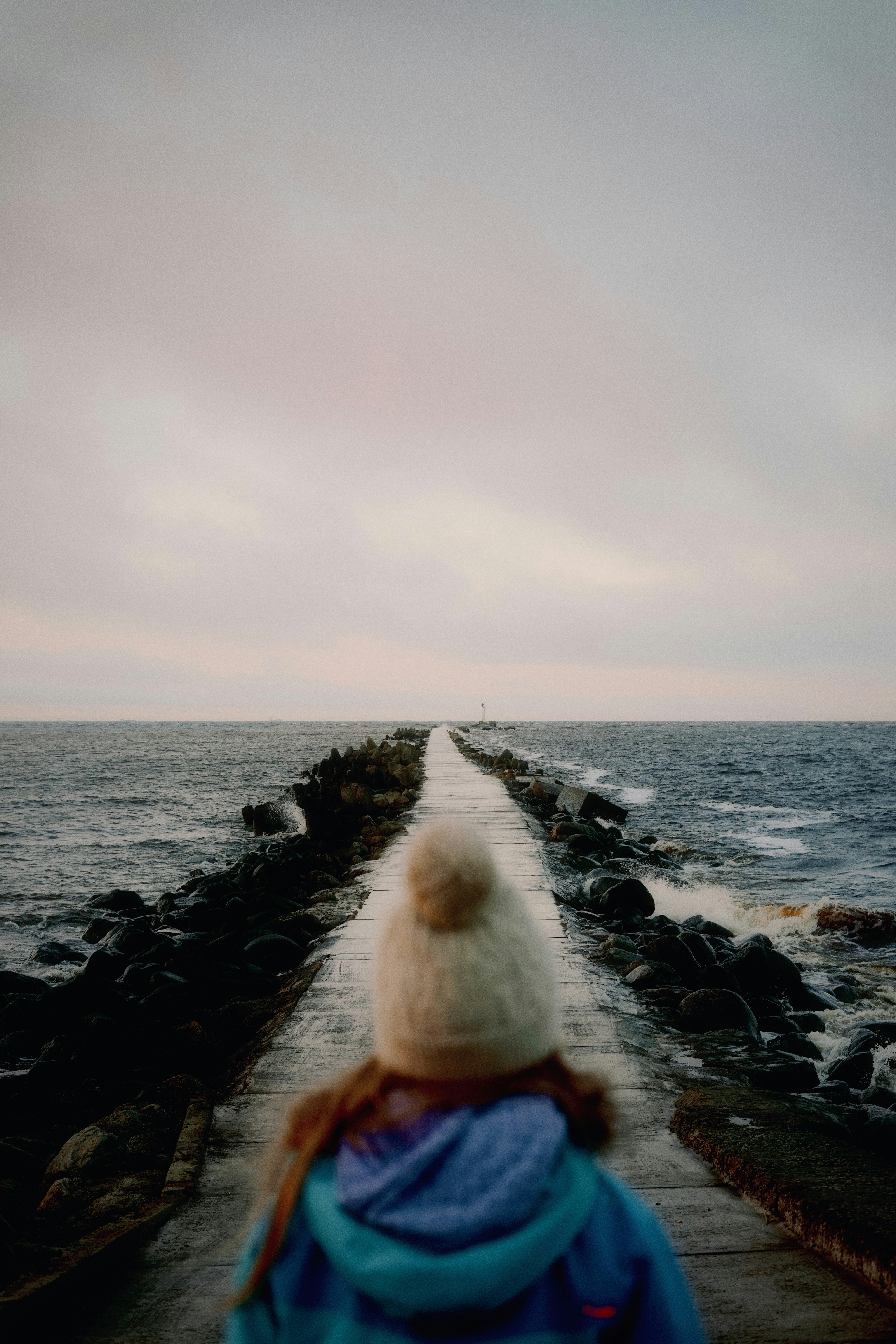 Person walks on a pier towards the ocean.