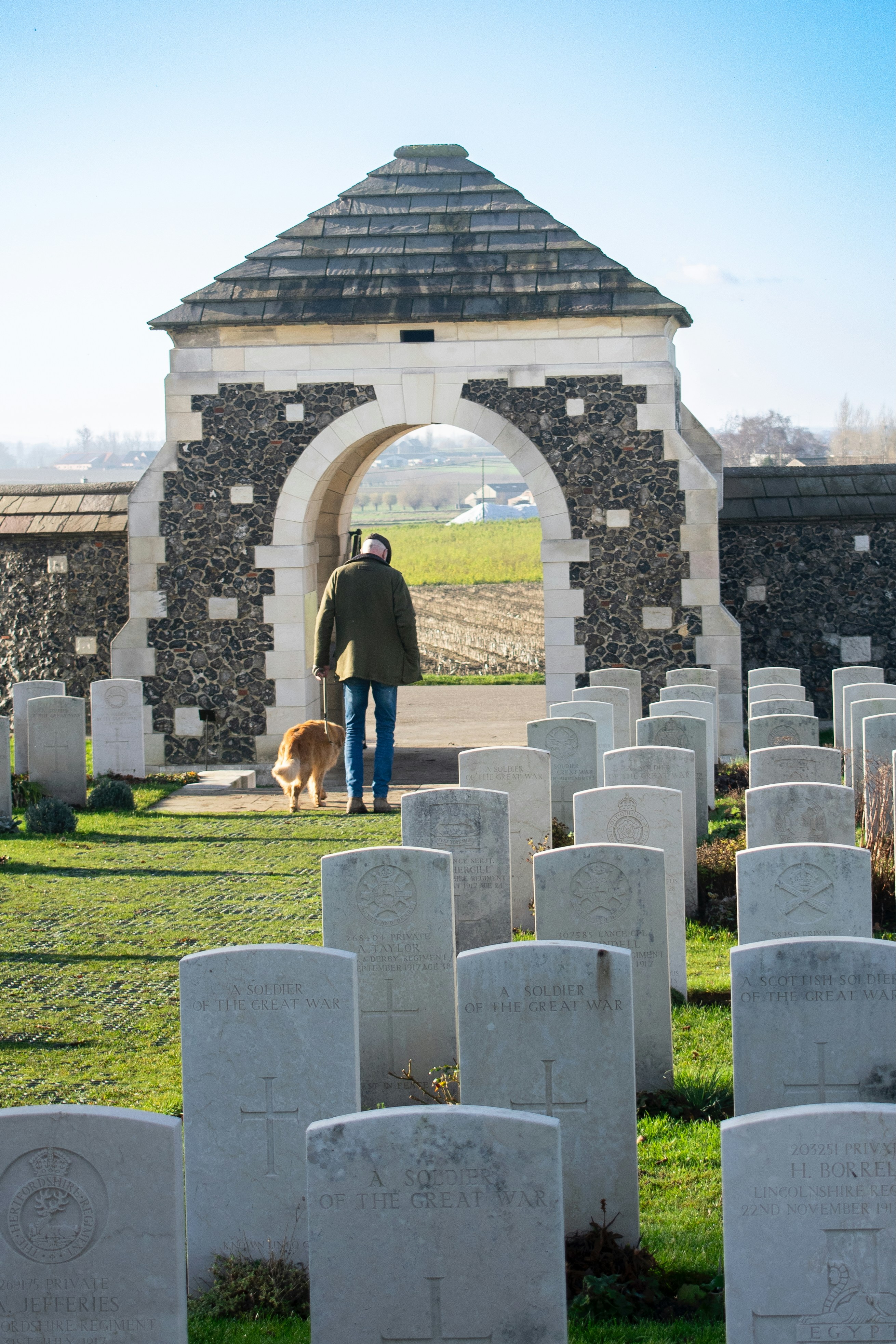Man and dog walk through war cemetery gate.