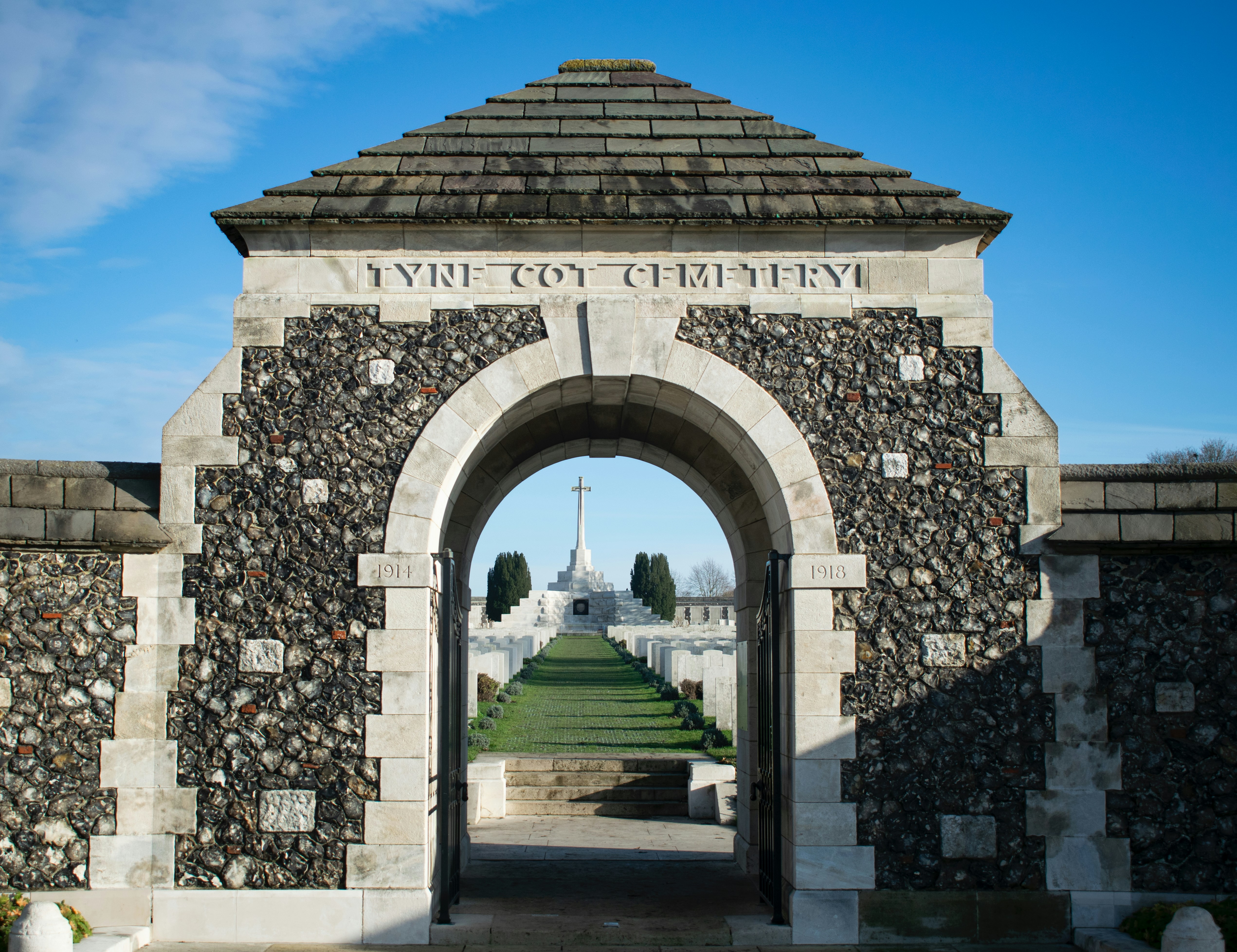 Stone archway leading to a war cemetery with cross