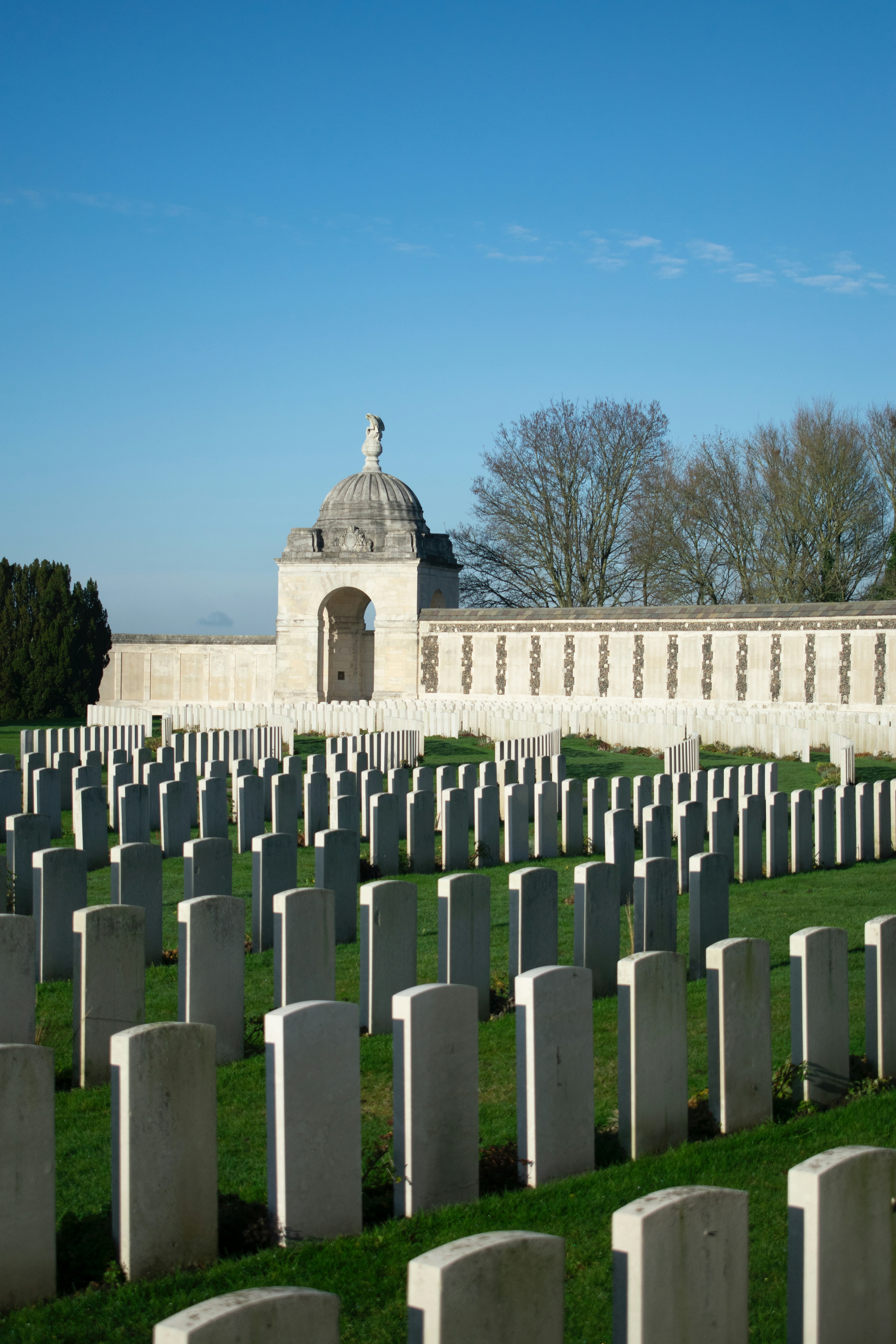 Rows of white headstones in a cemetery under blue sky.