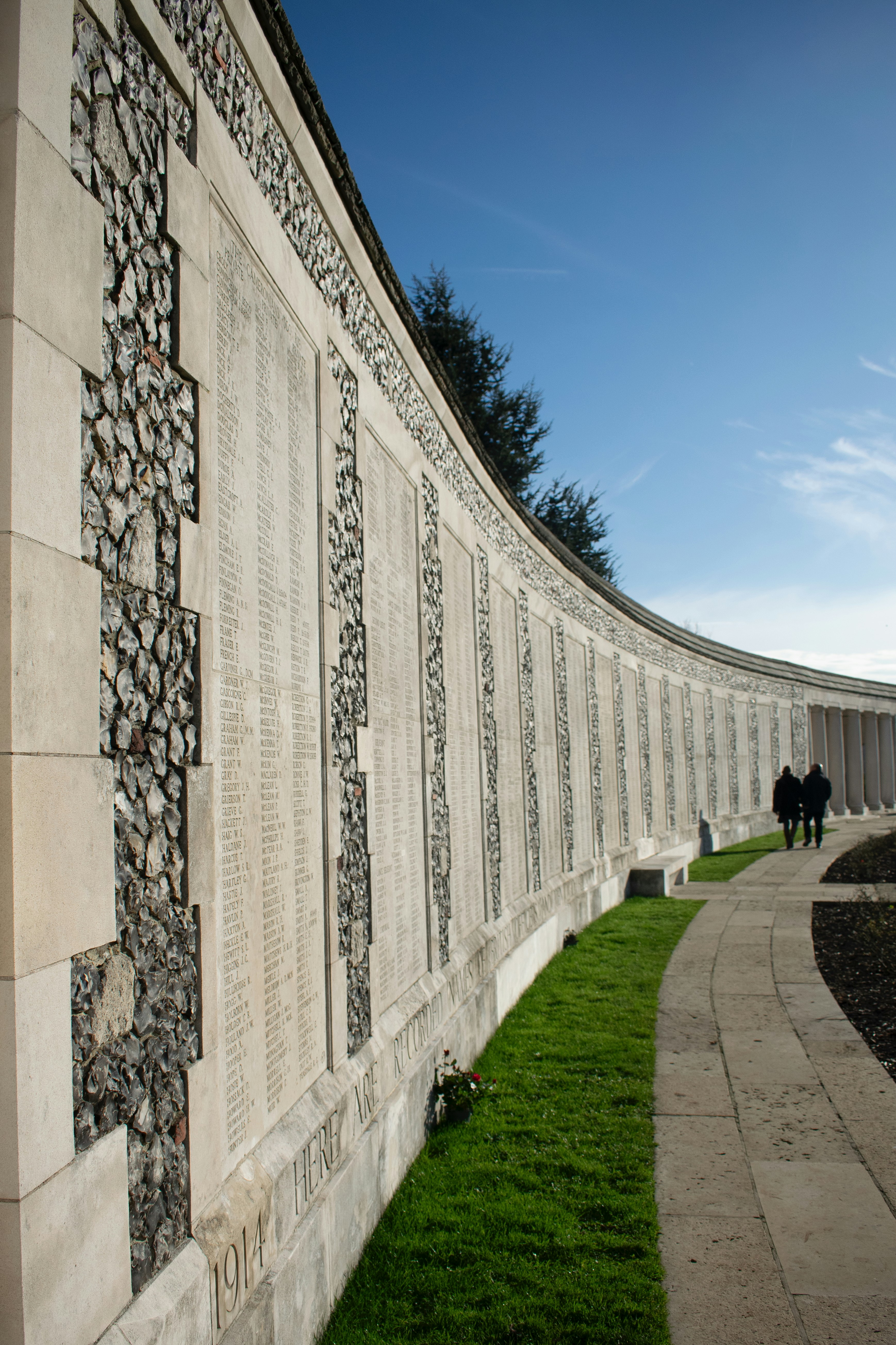 A curved memorial wall with names under a blue sky