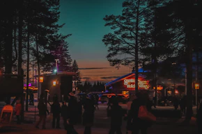 People walk through a village at dusk with colorful lights