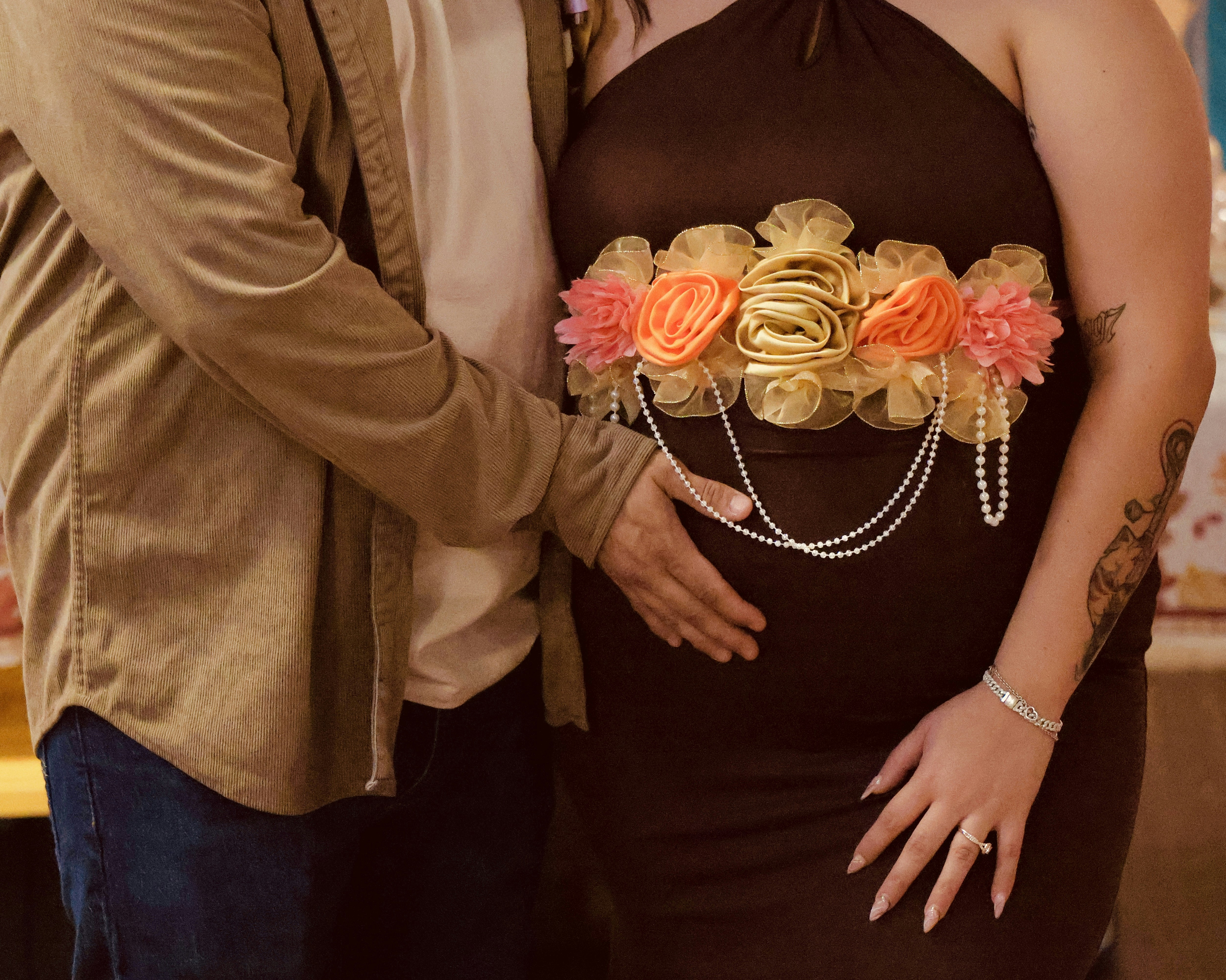 Pregnant woman with floral belly sash and partner's hand