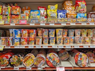 Shelves stocked with various instant noodle cups and snacks.