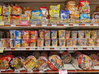 Shelves stocked with various instant noodle cups and snacks.