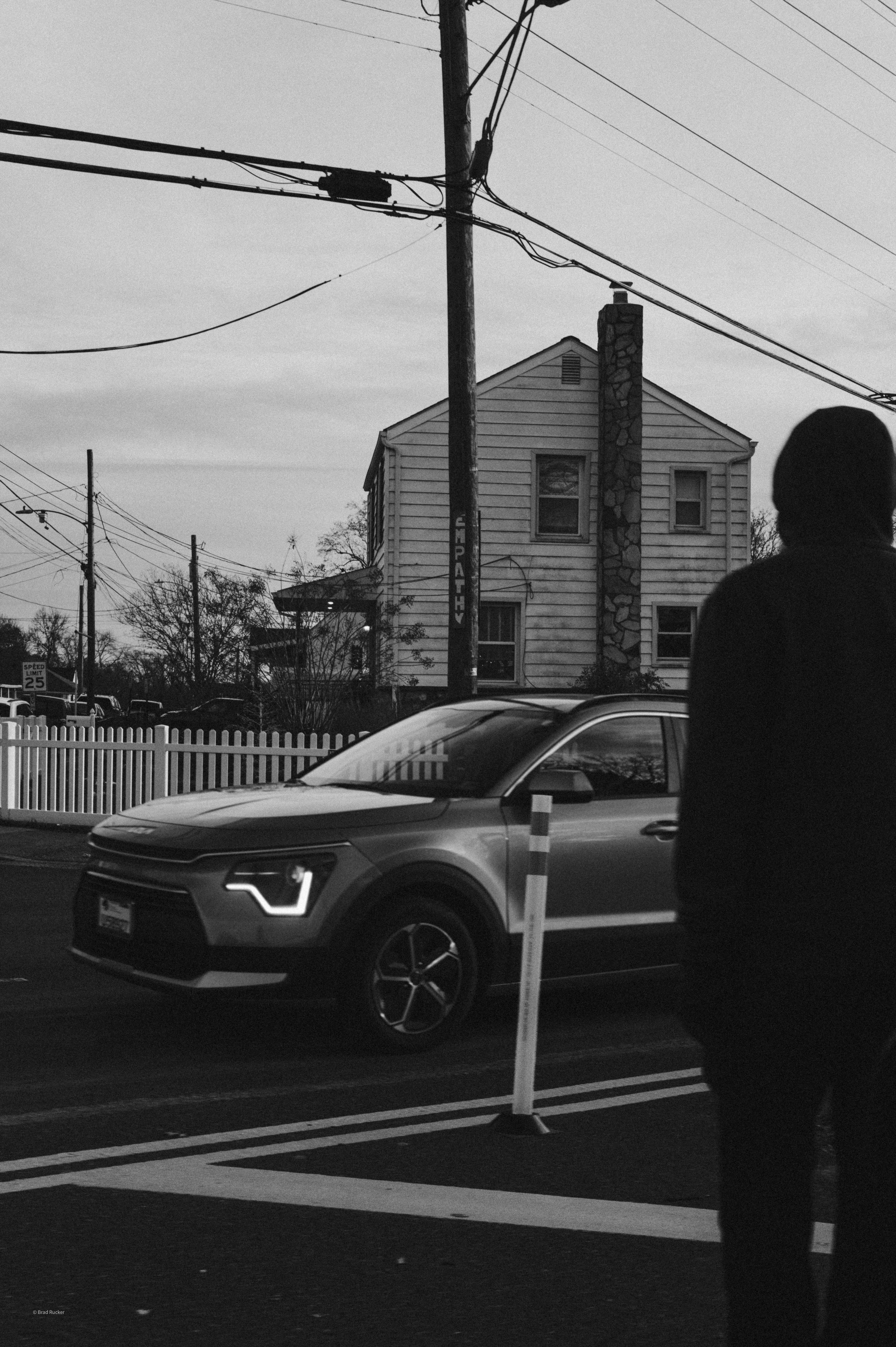 A car drives past a house with a person watching
