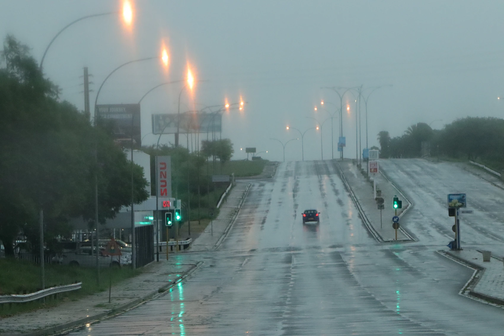 A rain-darkened Windhoek road with traffic lights reflected at dusk