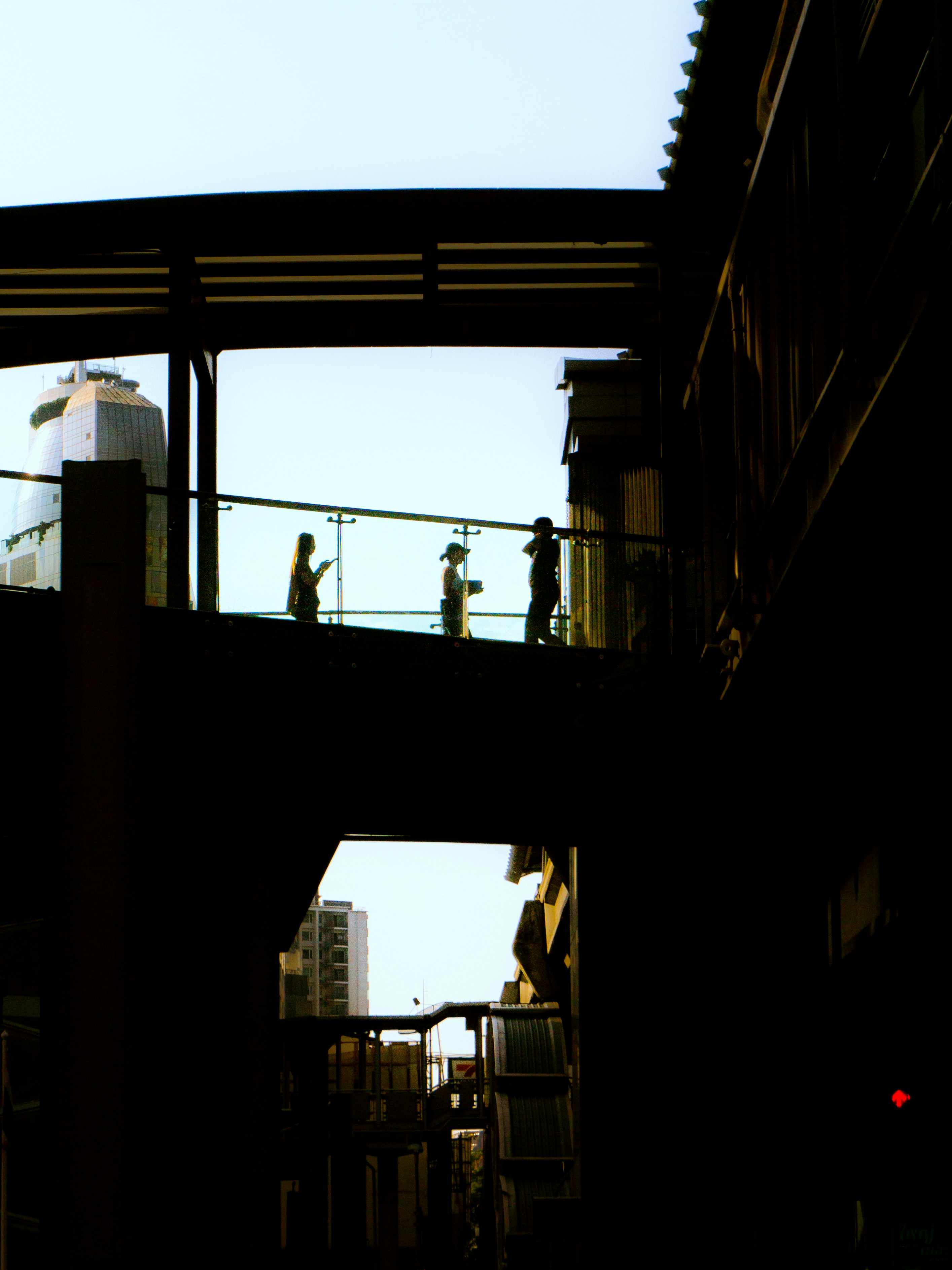 Silhouetten von Menschen auf einem Skywalk gegen den Himmel.