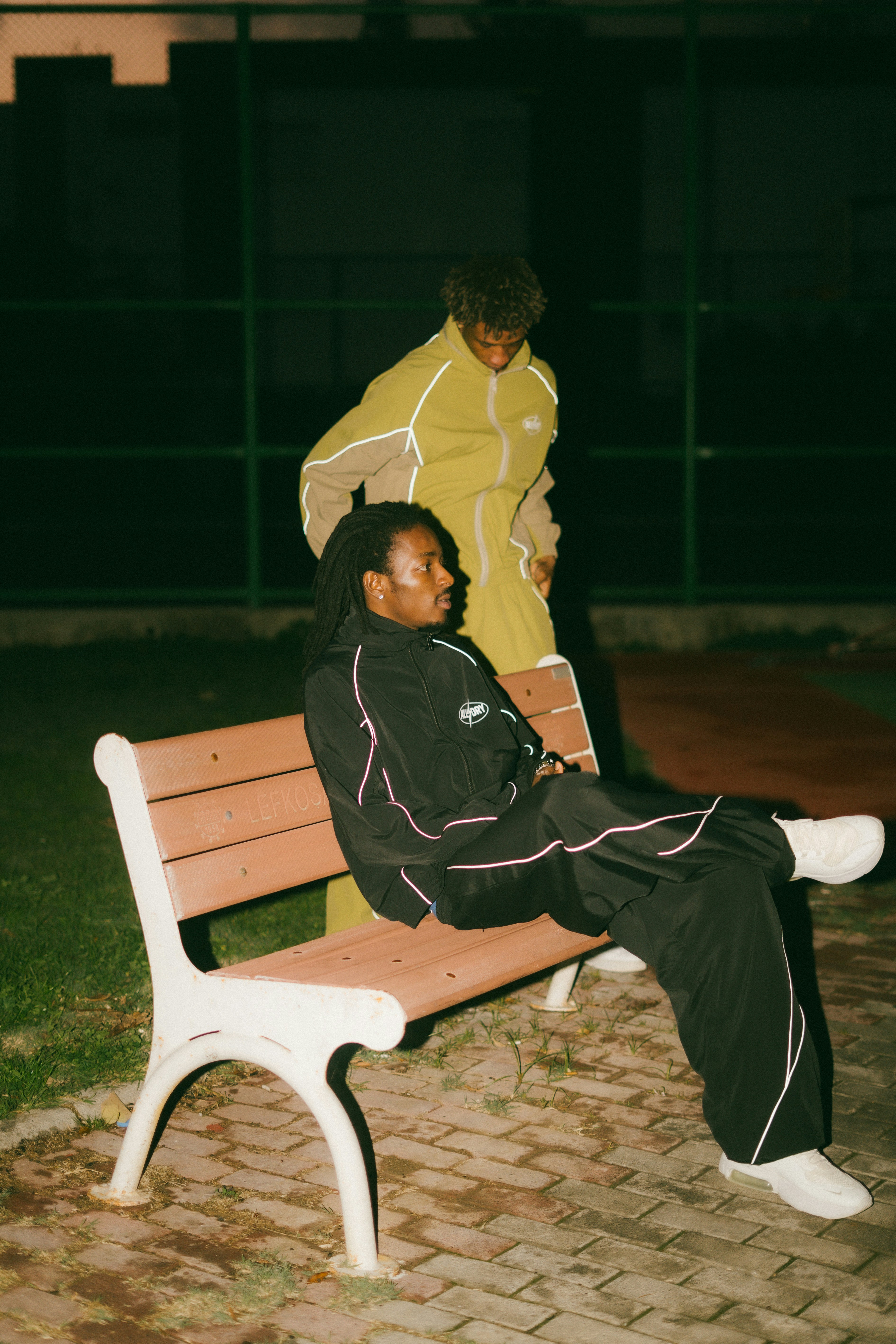 Two young men in tracksuits sitting on a park bench.