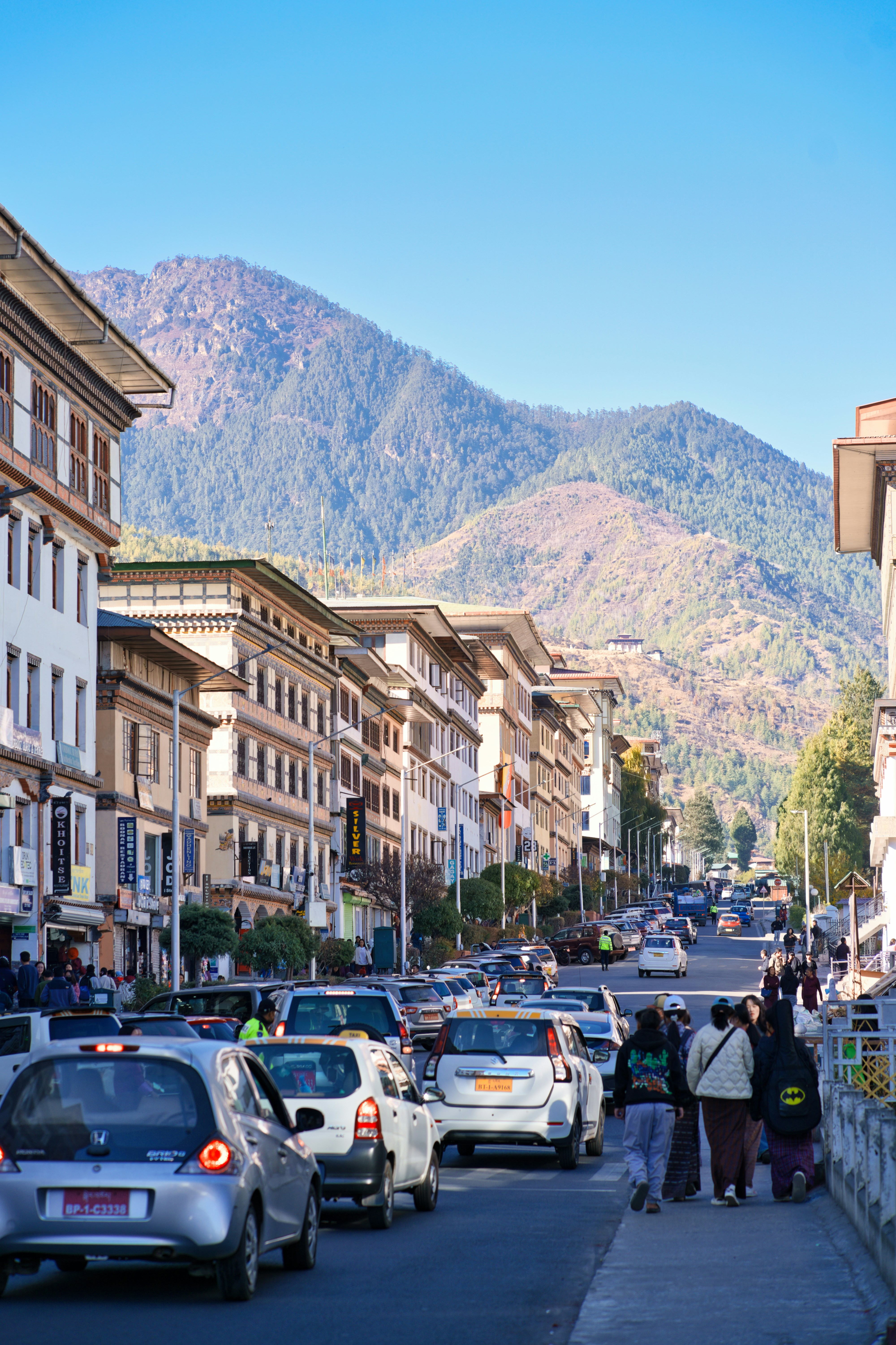 Busy street with cars and buildings against mountains.