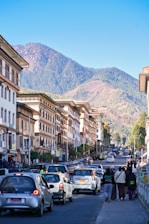 Busy street with cars and buildings against mountains.