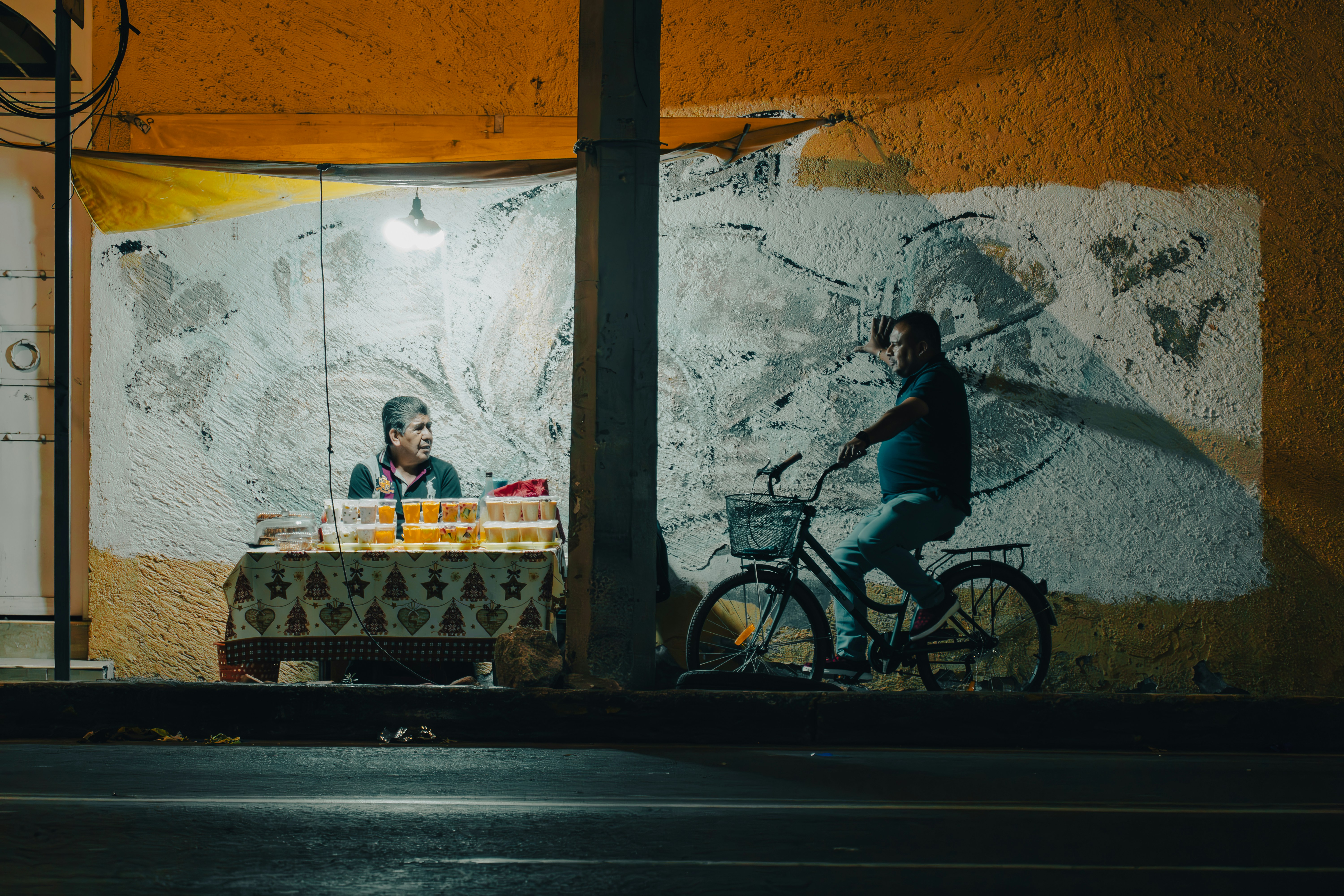 Man rides bicycle past illuminated stall at night