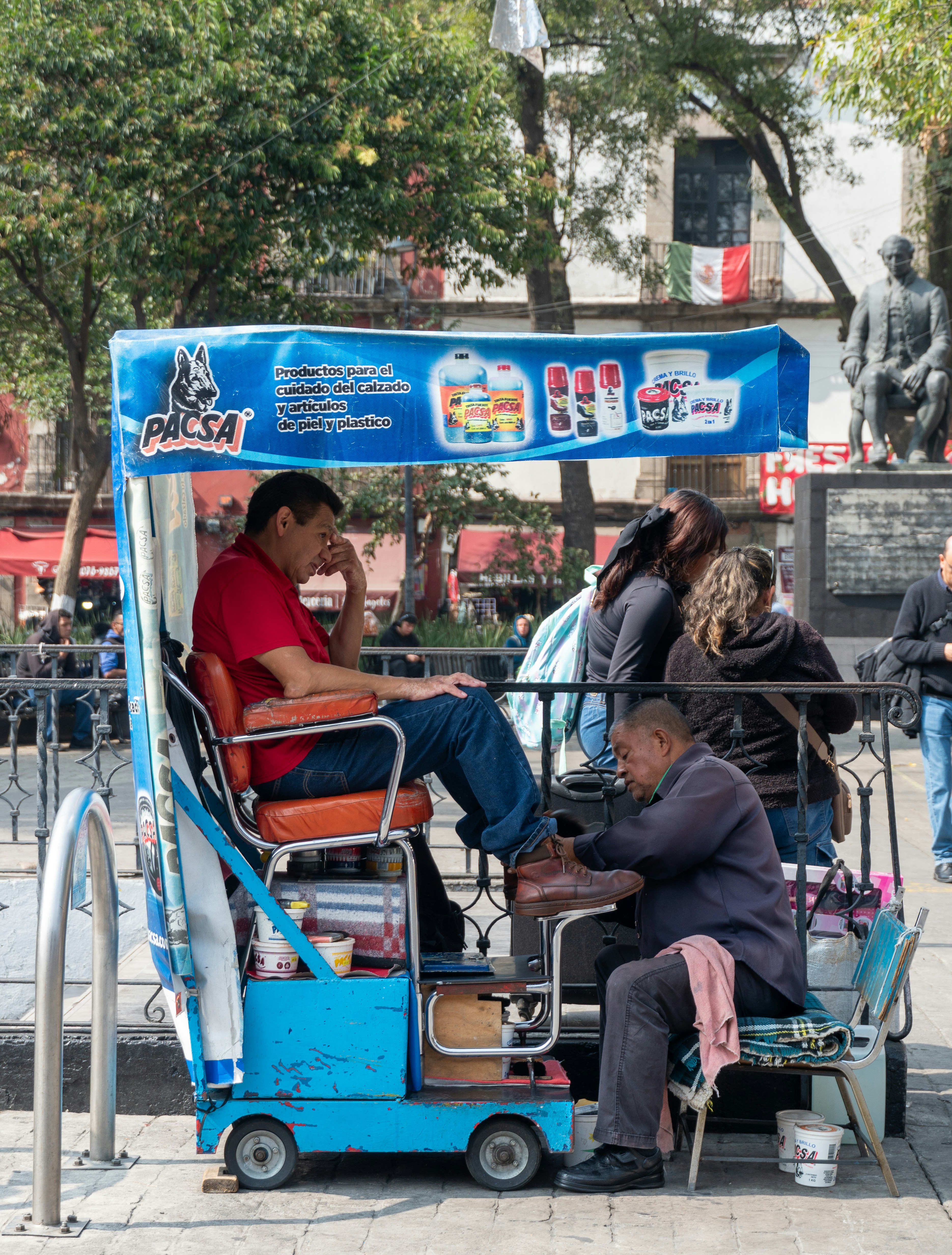 Man shining shoes in a blue cart with customers