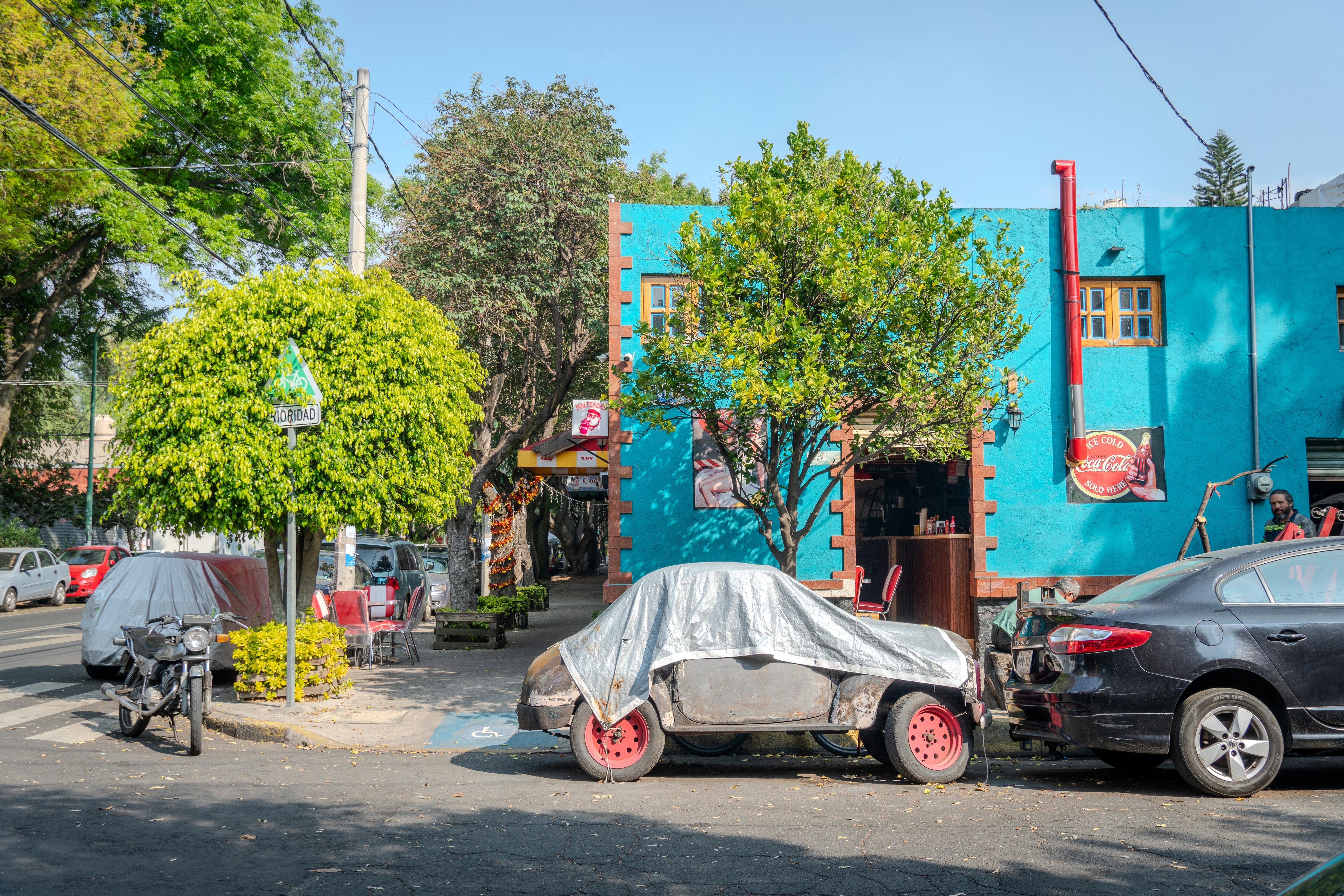 Cars covered and parked on a sunny street.