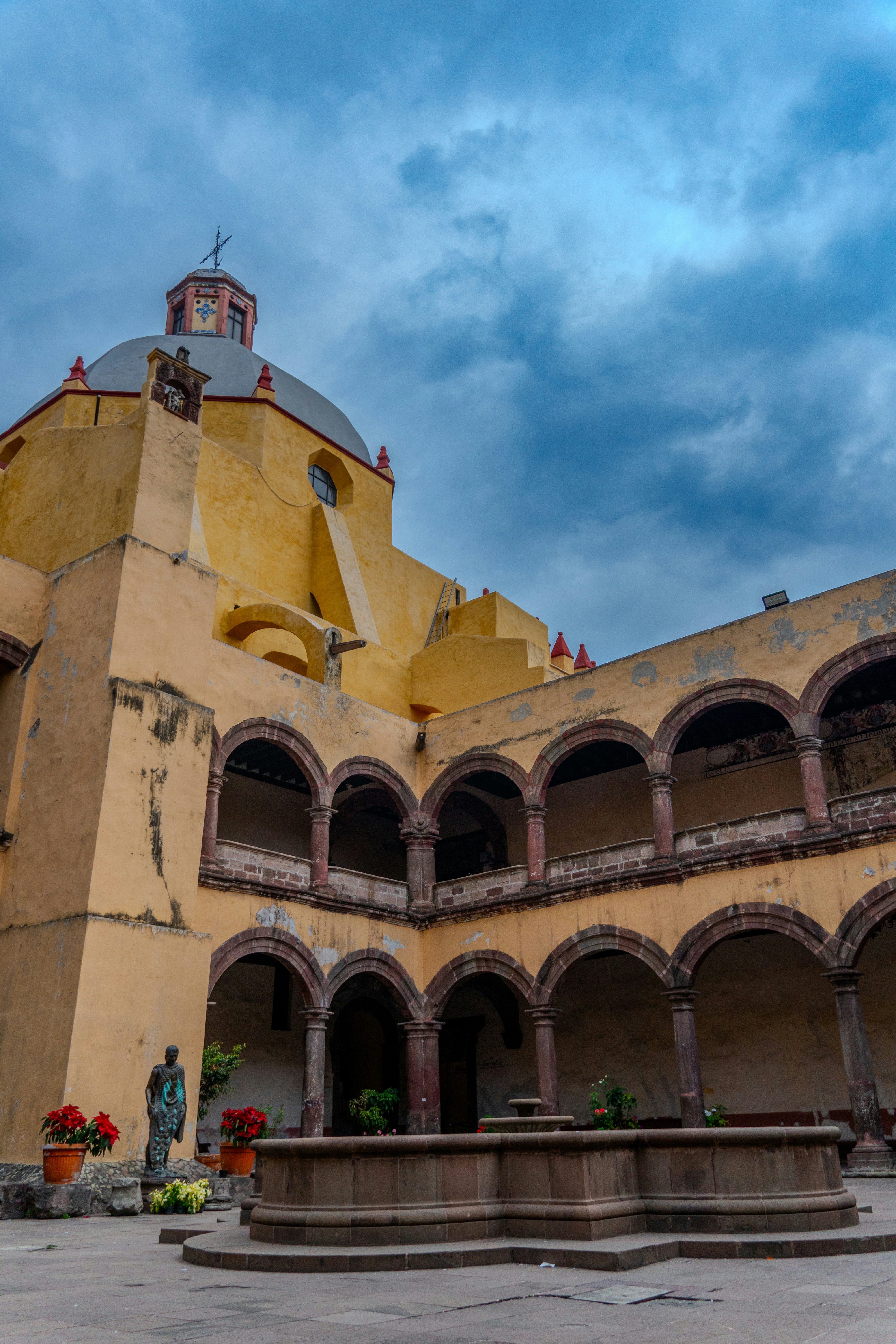 Courtyard with arches and fountain under cloudy sky