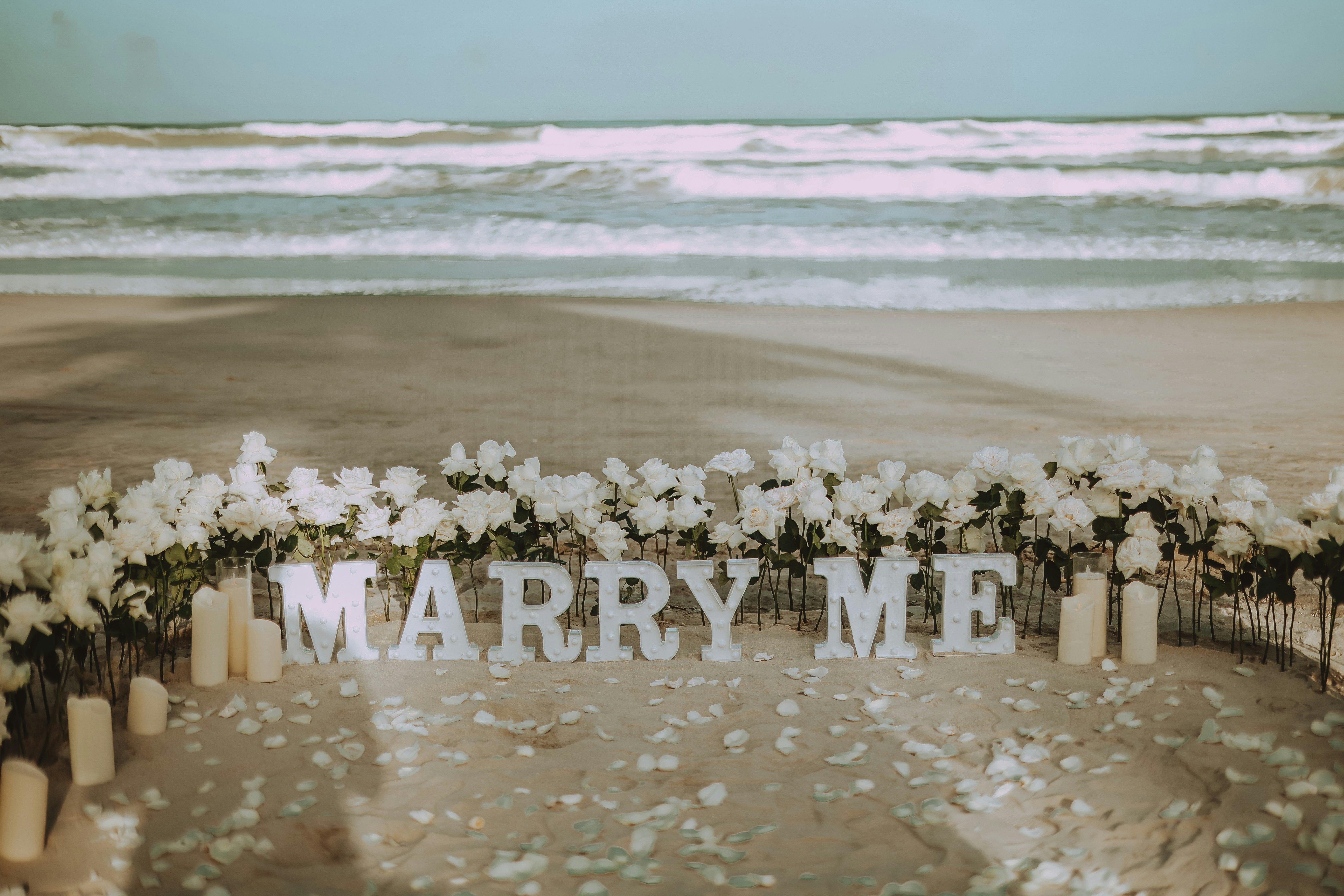 Marry me sign on a beach with flowers