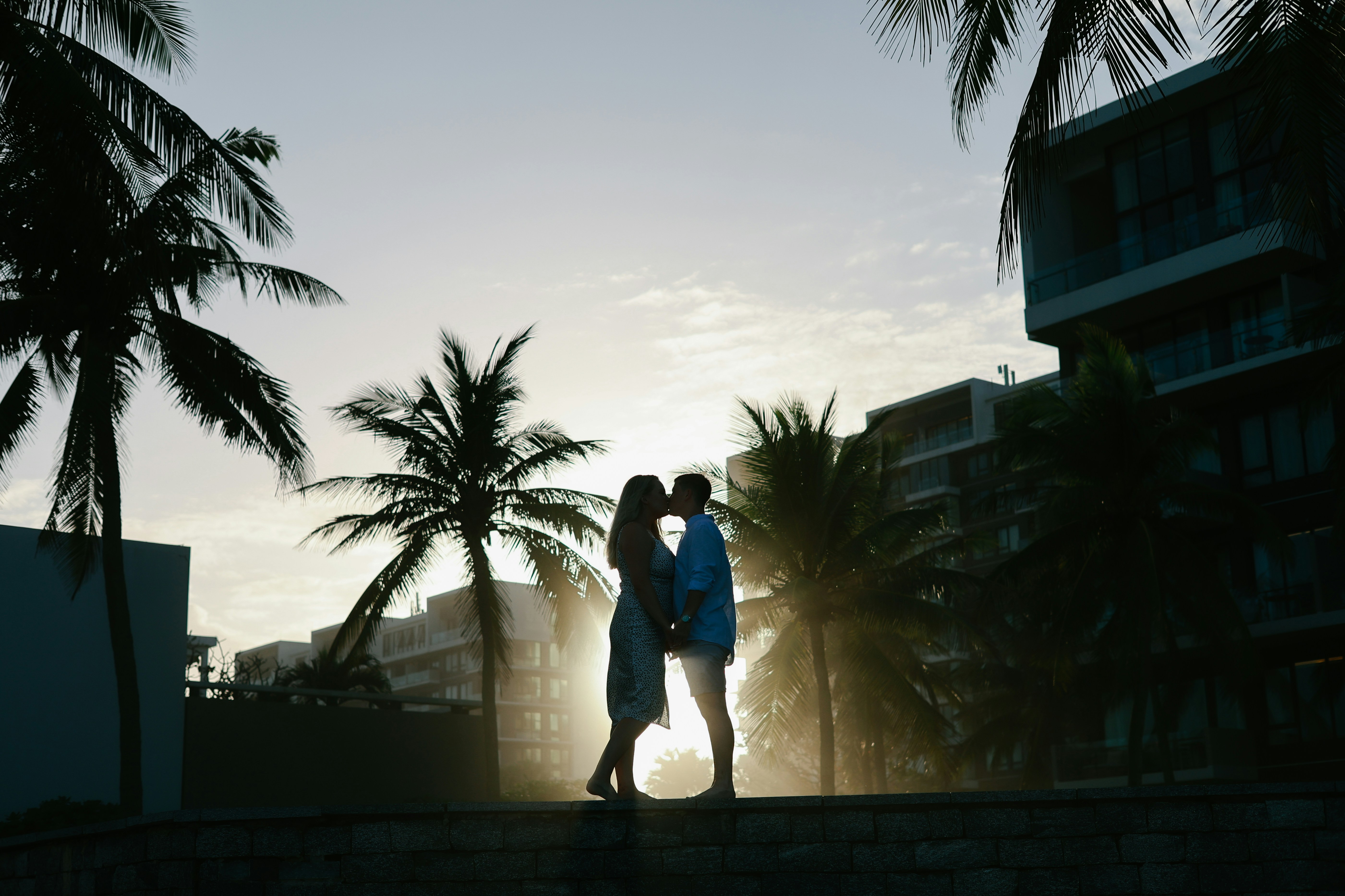 Couple kissing at sunset with palm trees and buildings