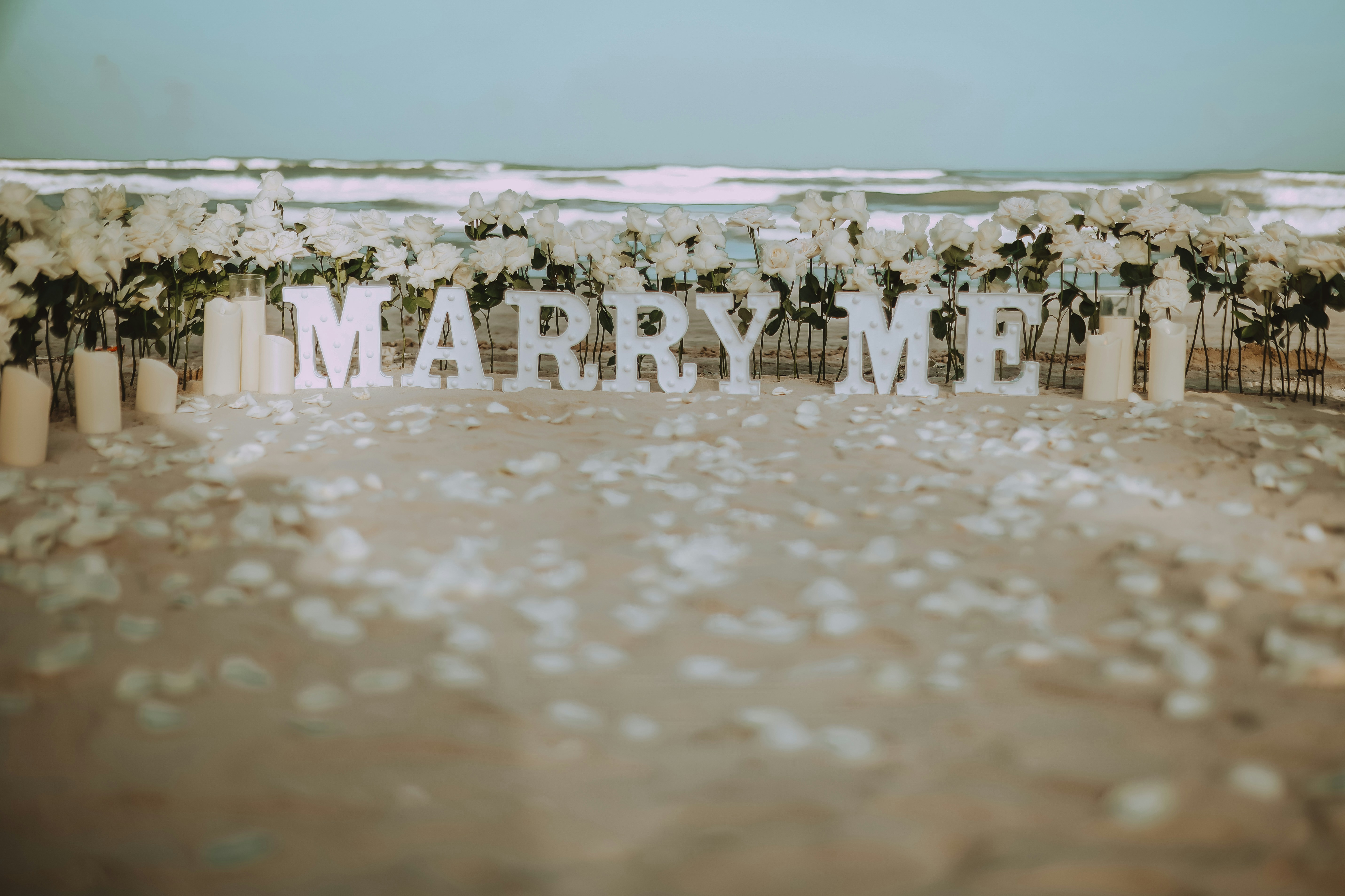 Marry me sign on a beach with flowers