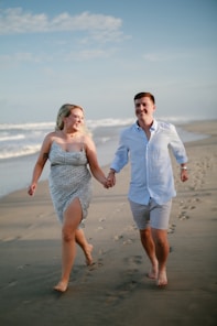 A couple holding hands running on a beach.