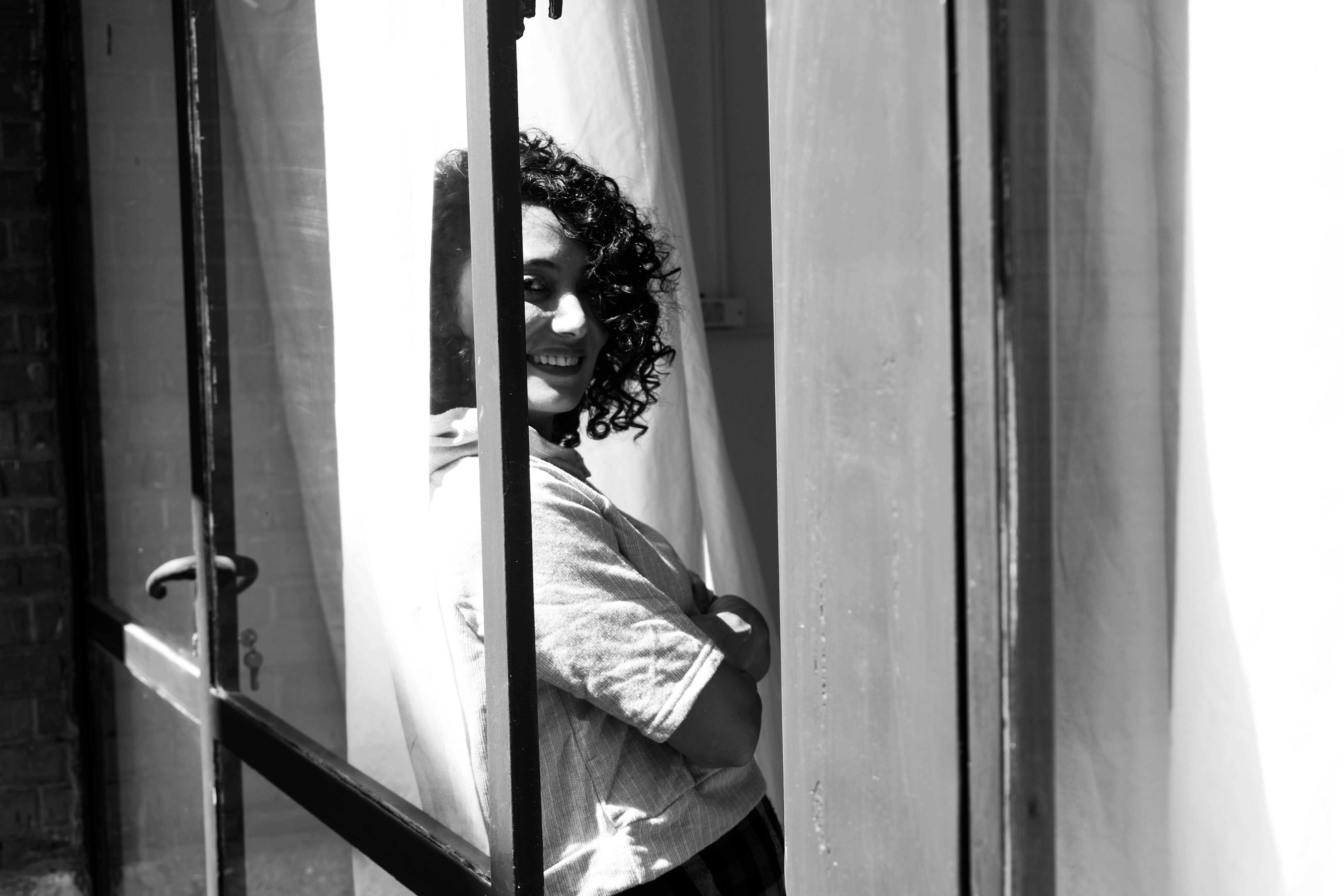 A smiling woman with curly hair looks through window