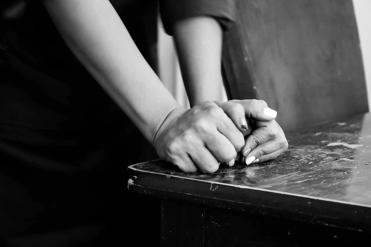 A pair of hands resting clasped on a worn table top
