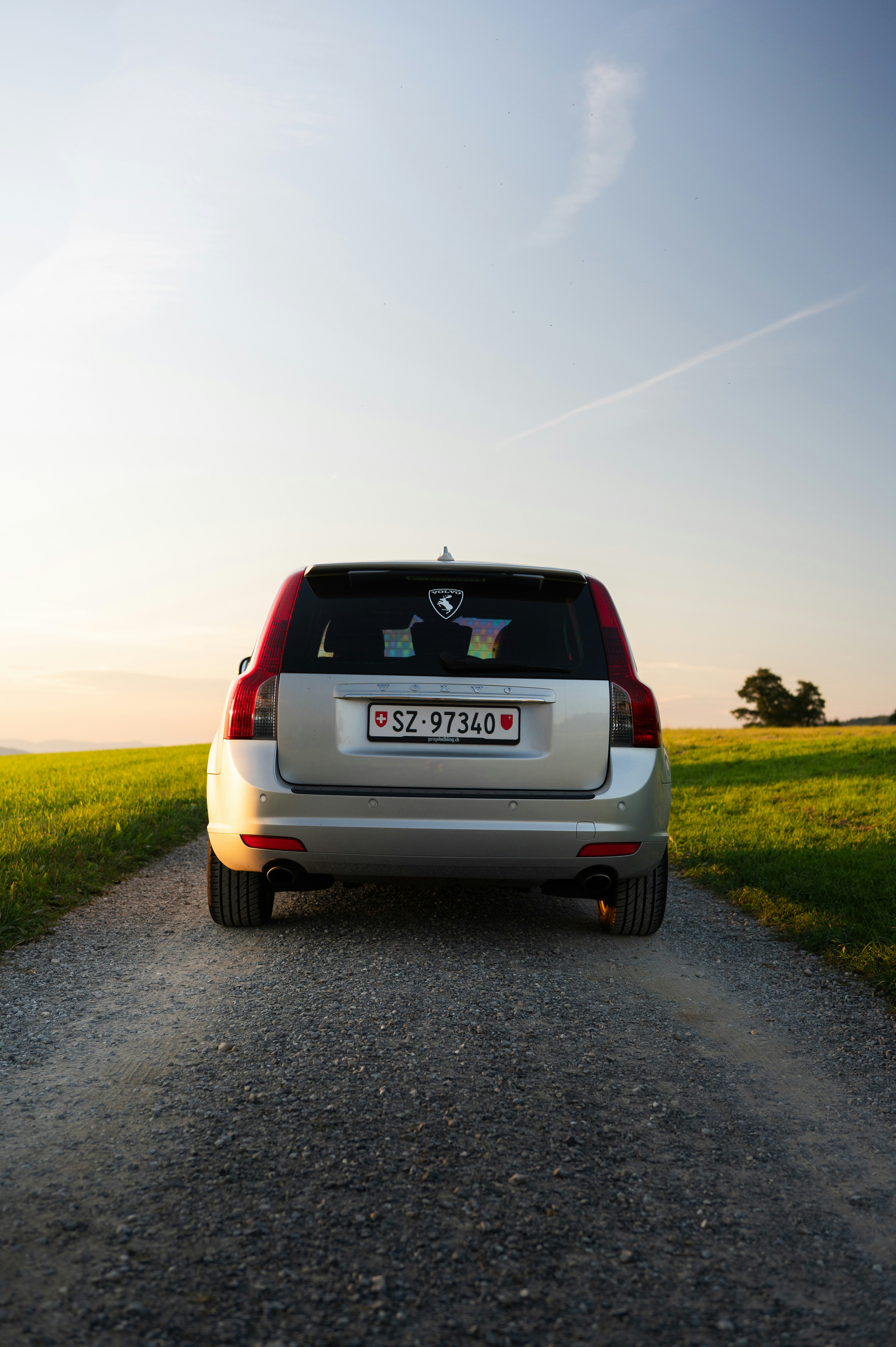 Silver car parked on a gravel road at sunset.