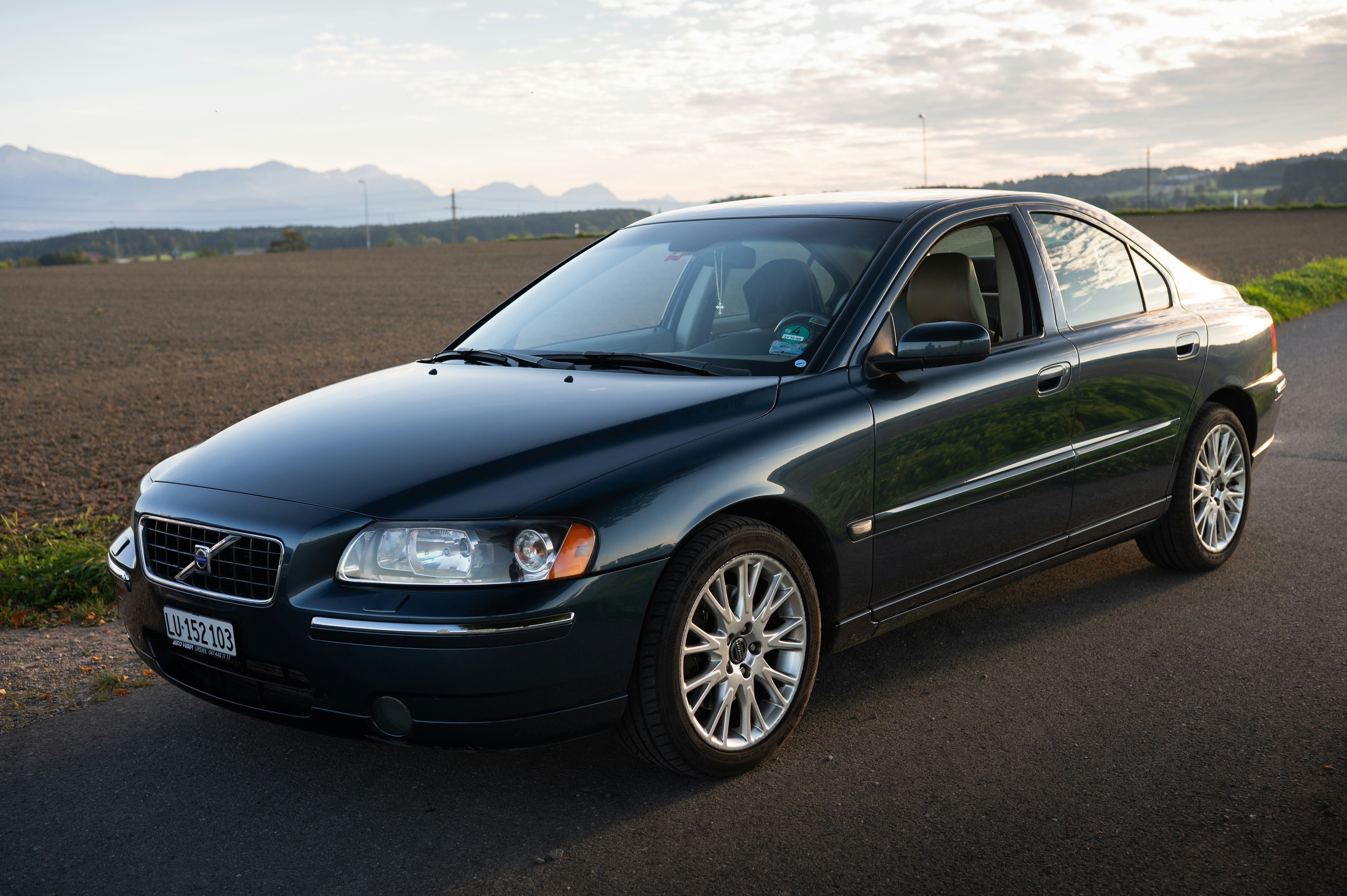 Dark green volvo sedan parked on a road.