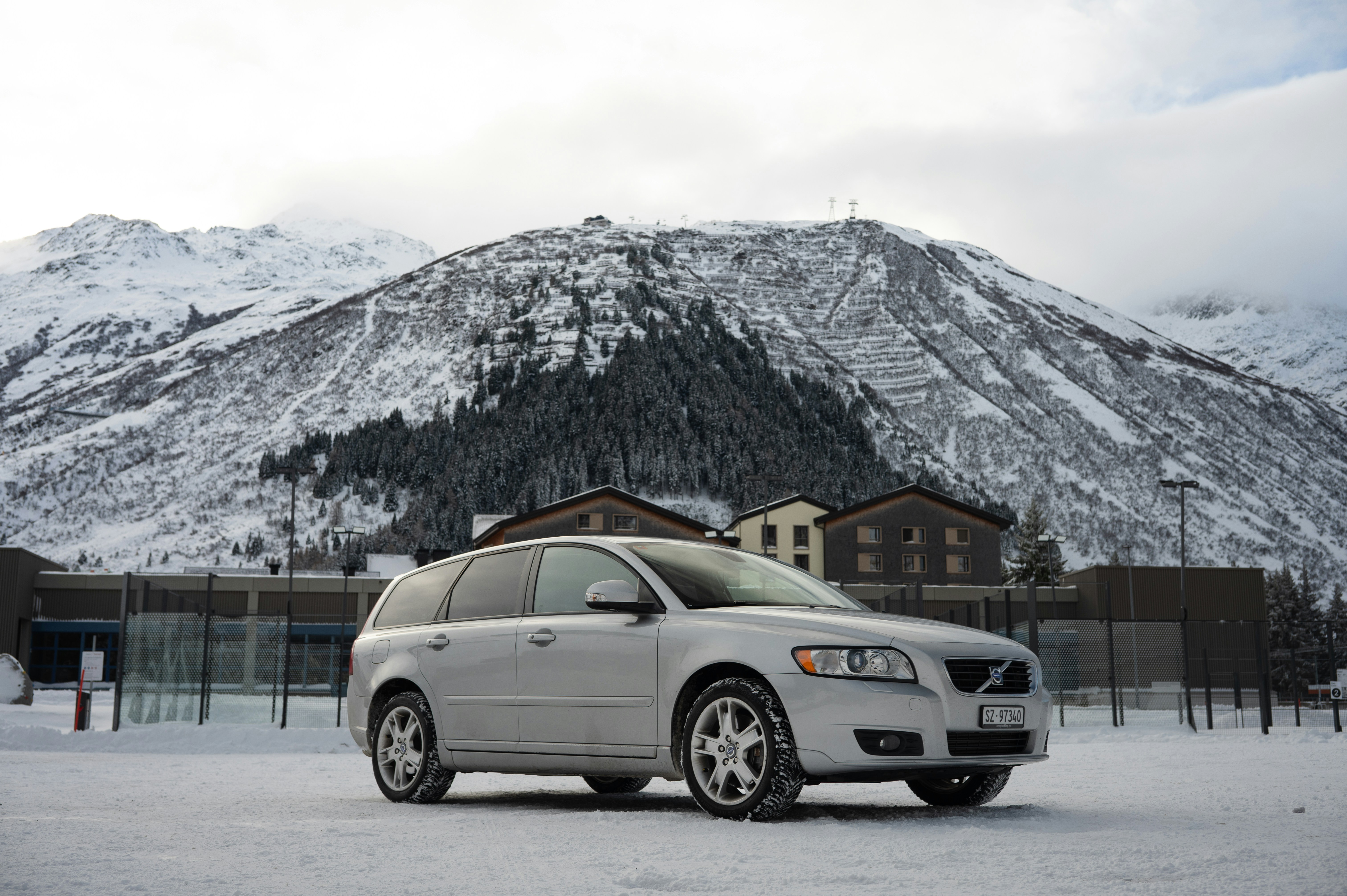 Silver volvo station wagon parked in snowy mountain landscape.