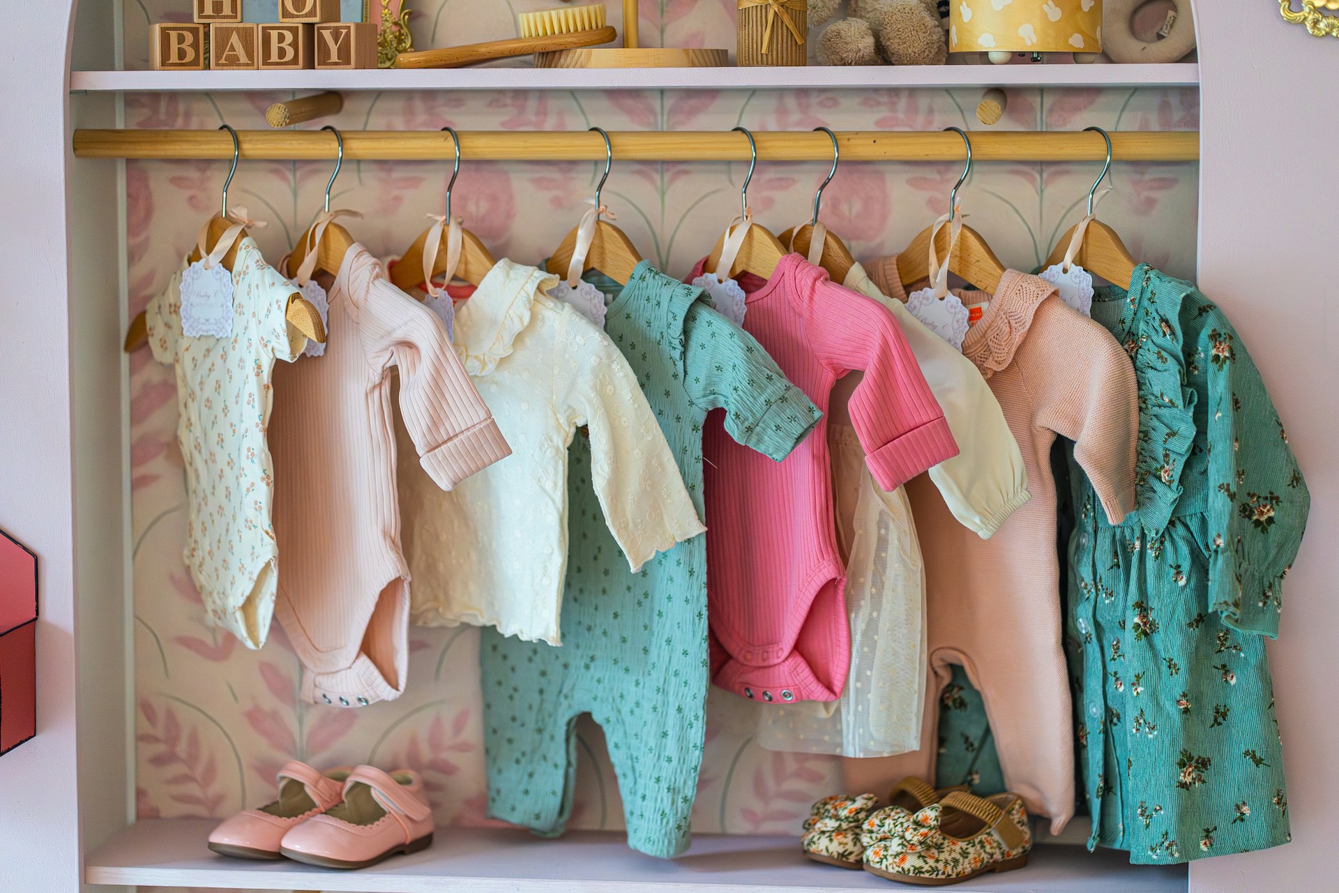 Baby clothes hanging on a rack with shoes below shoes.