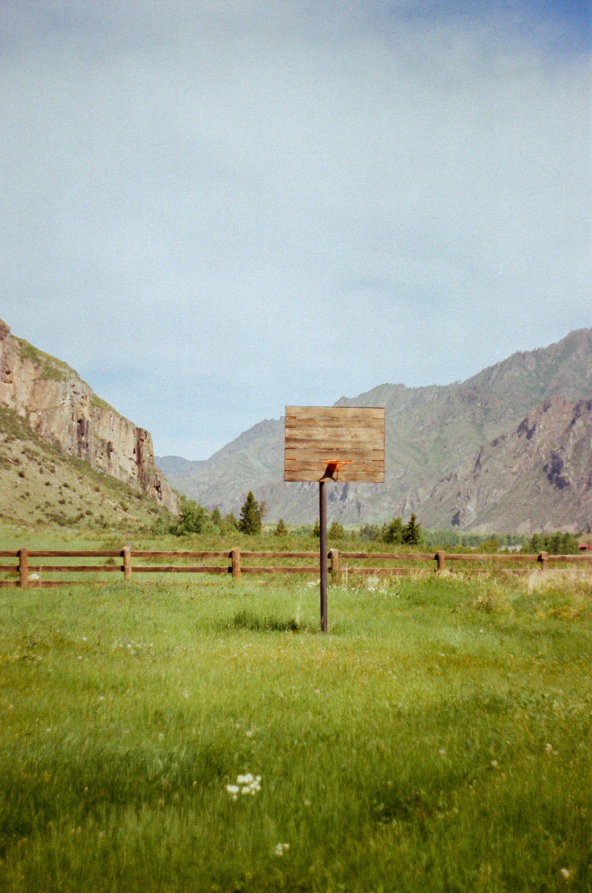 Wooden basketball hoop in a grassy field with mountains.