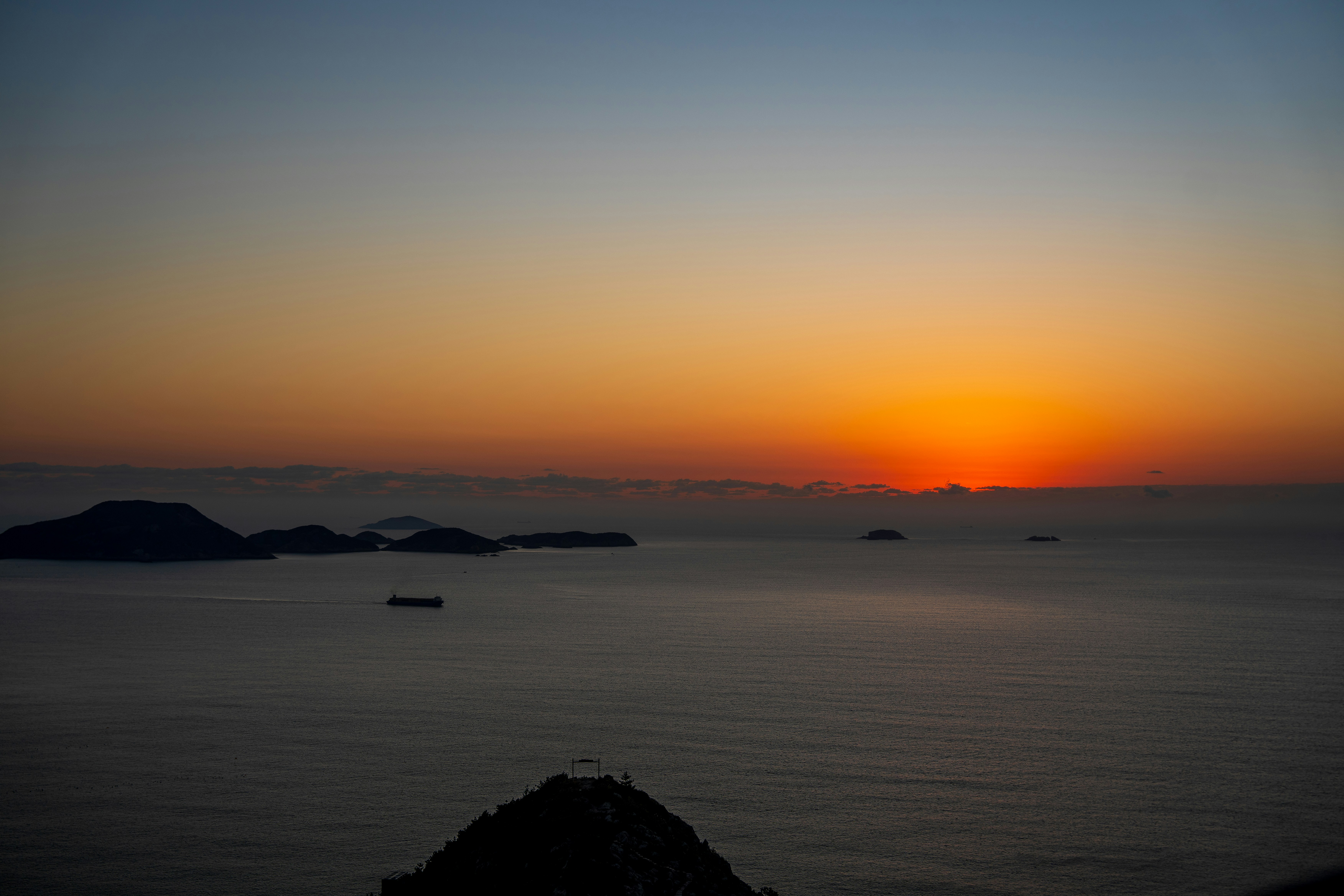 Sonnenaufgang über dem Ozean mit Inseln und Schiffen.