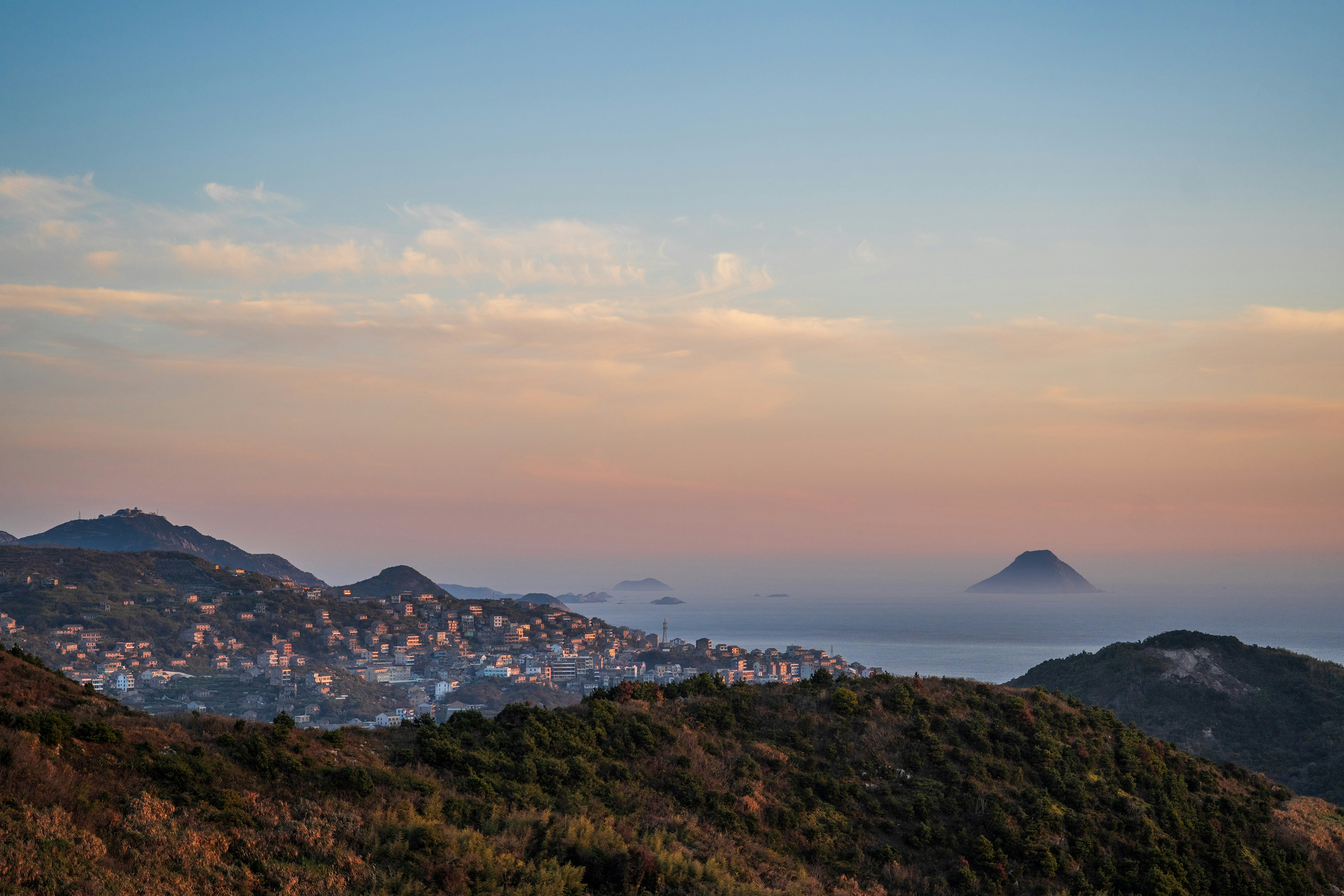 Hügel mit Blick auf eine Küstenstadt bei Sonnenuntergang.