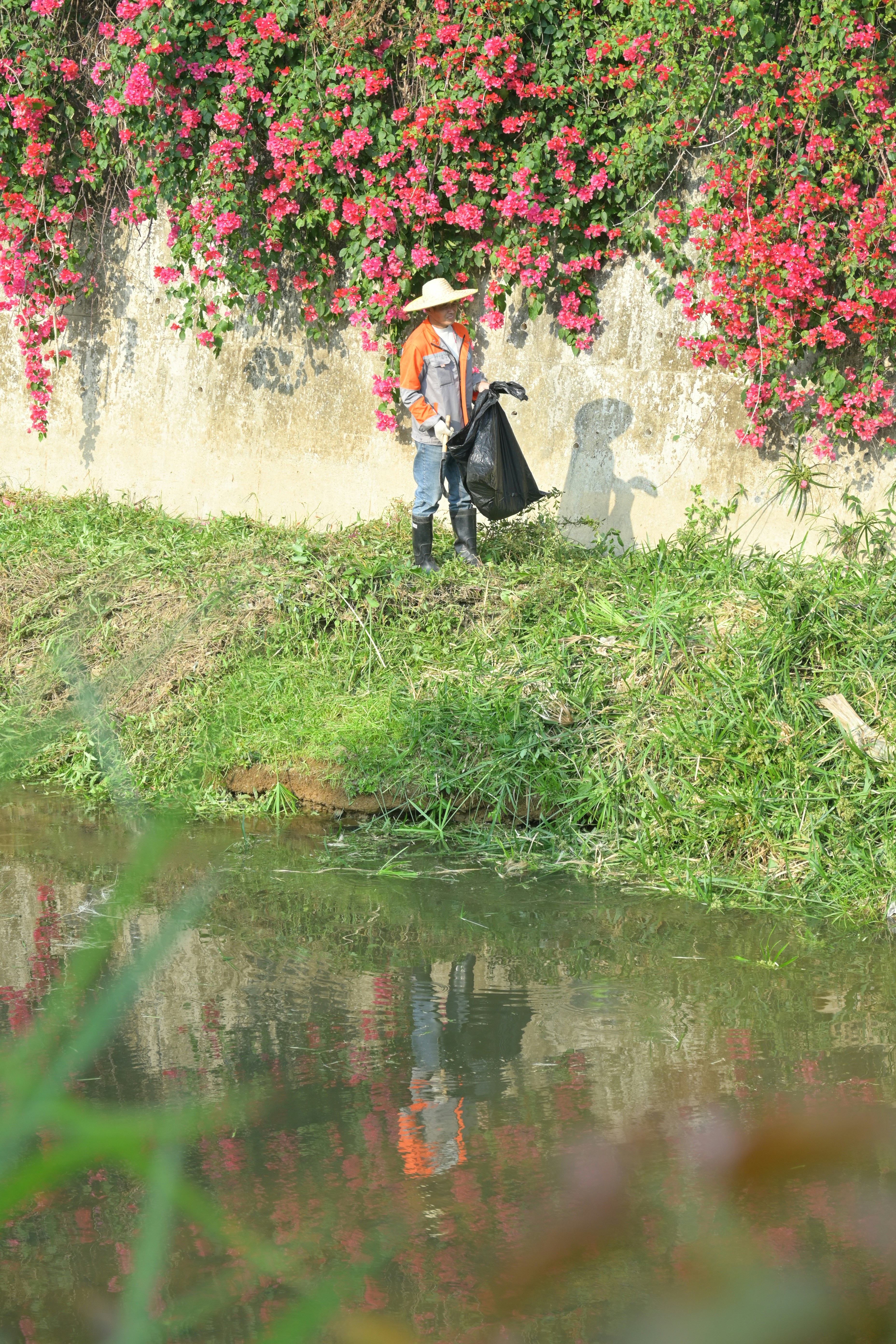 Person with trash bag near wall with flowers