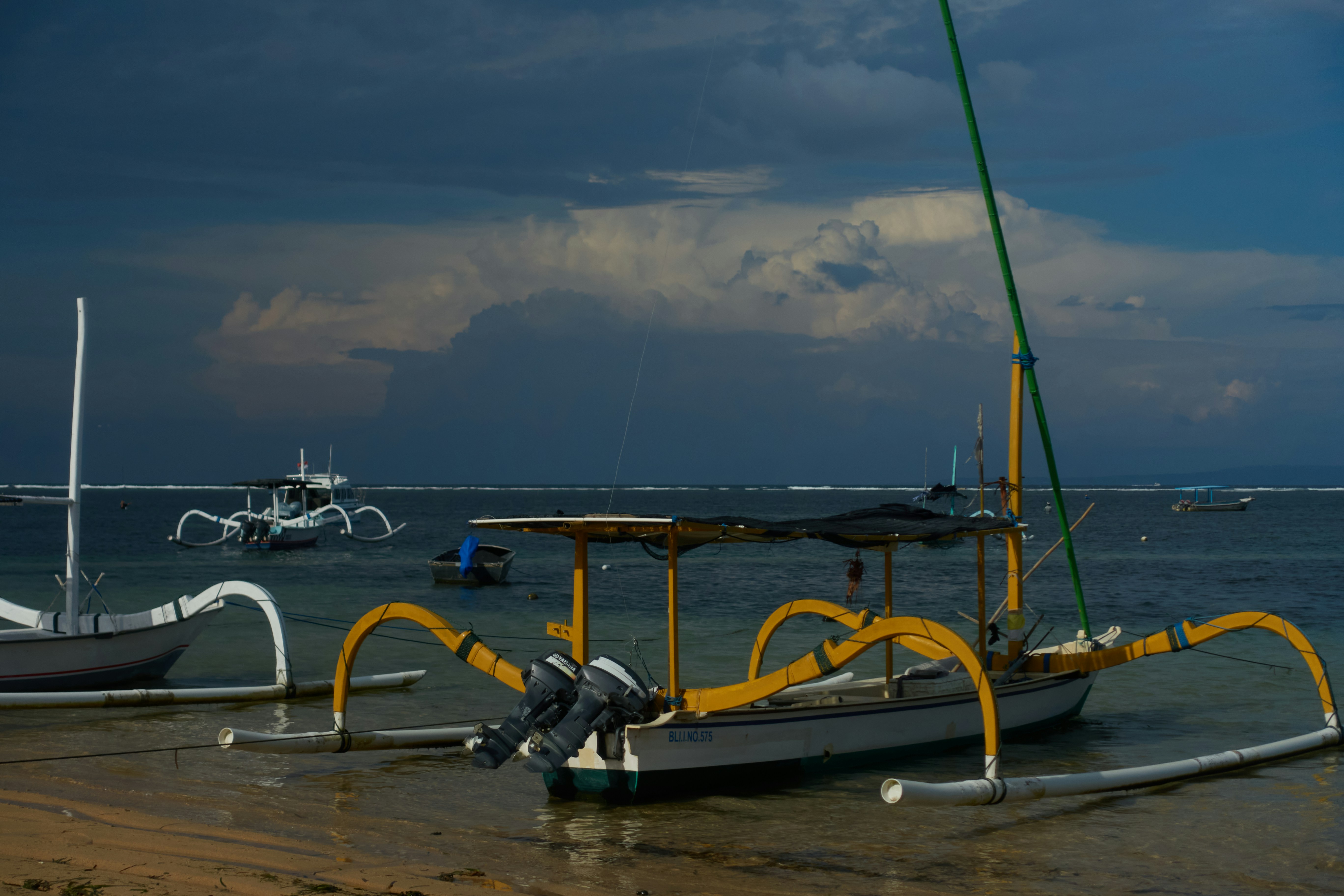 Traditional balinese fishing boats rest on a sandy shore.