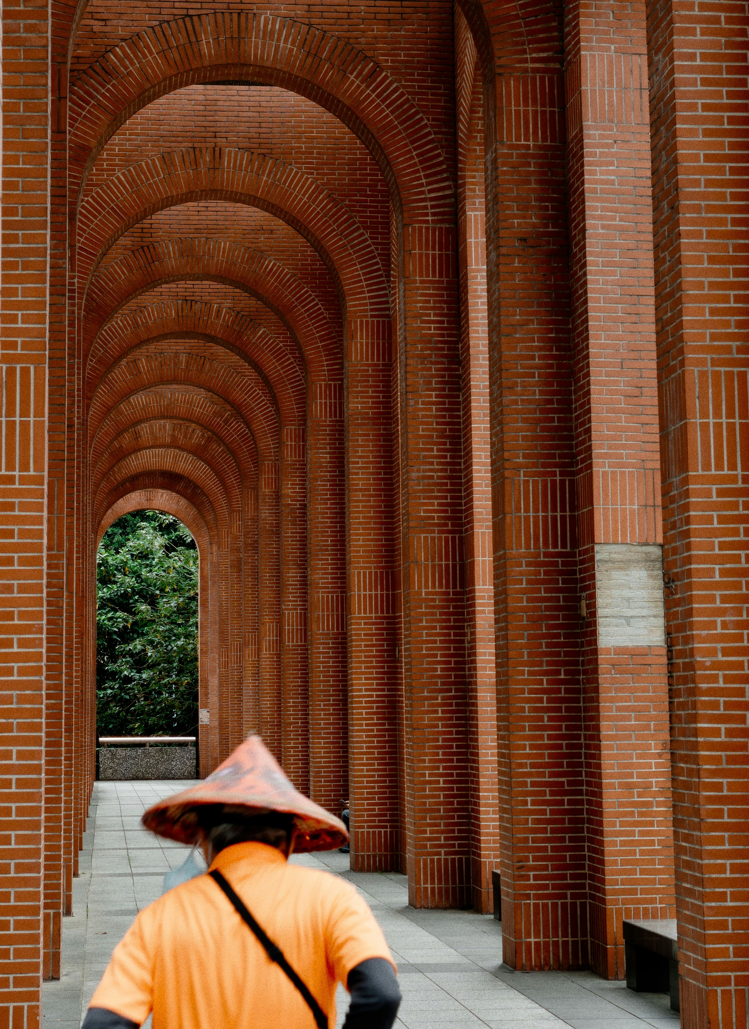 Person in conical hat walks through brick archway