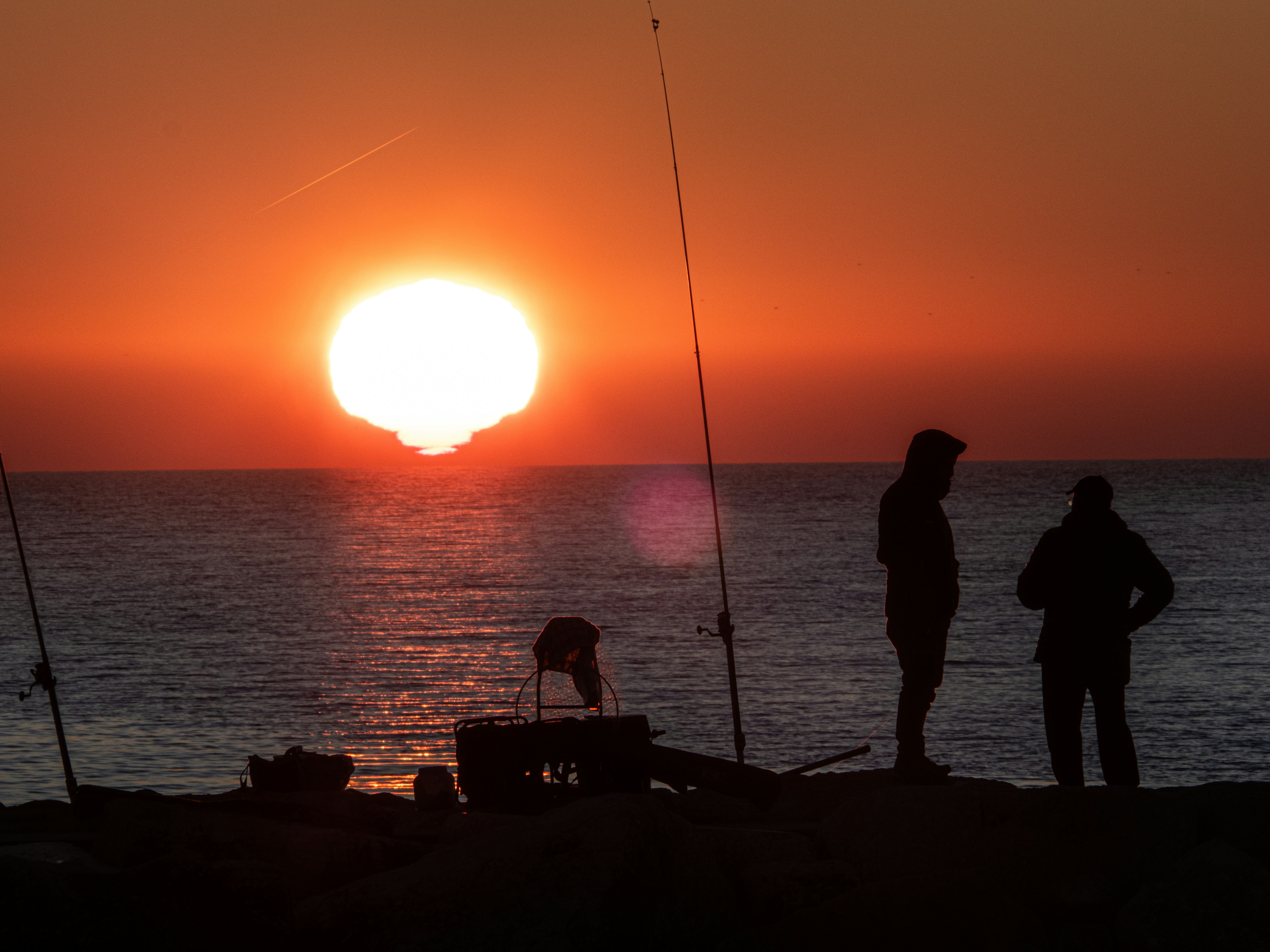 Two people fishing by the ocean at sunrise
