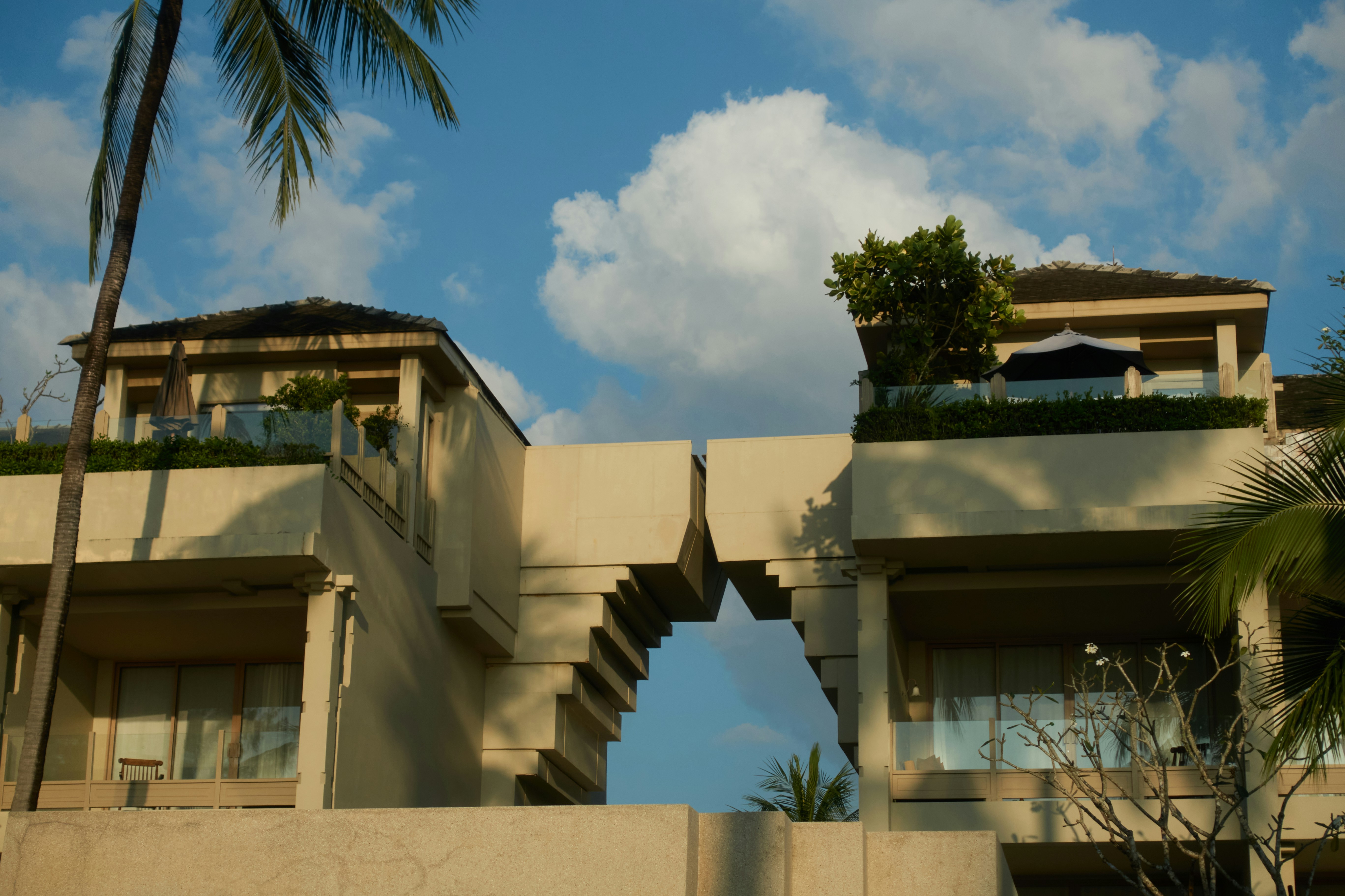 Modern resort buildings with arched walkway and palm trees.