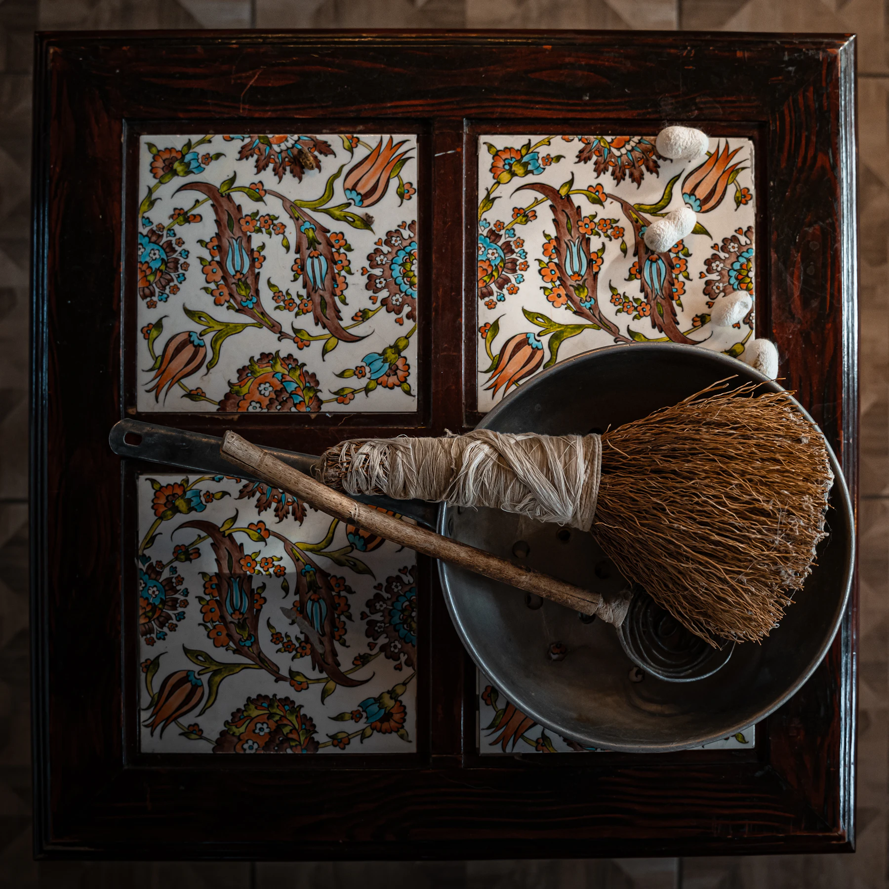 A metal basin holding a straw brush wound with raw silk, with white cocoons resting on a painted tile tray beside it