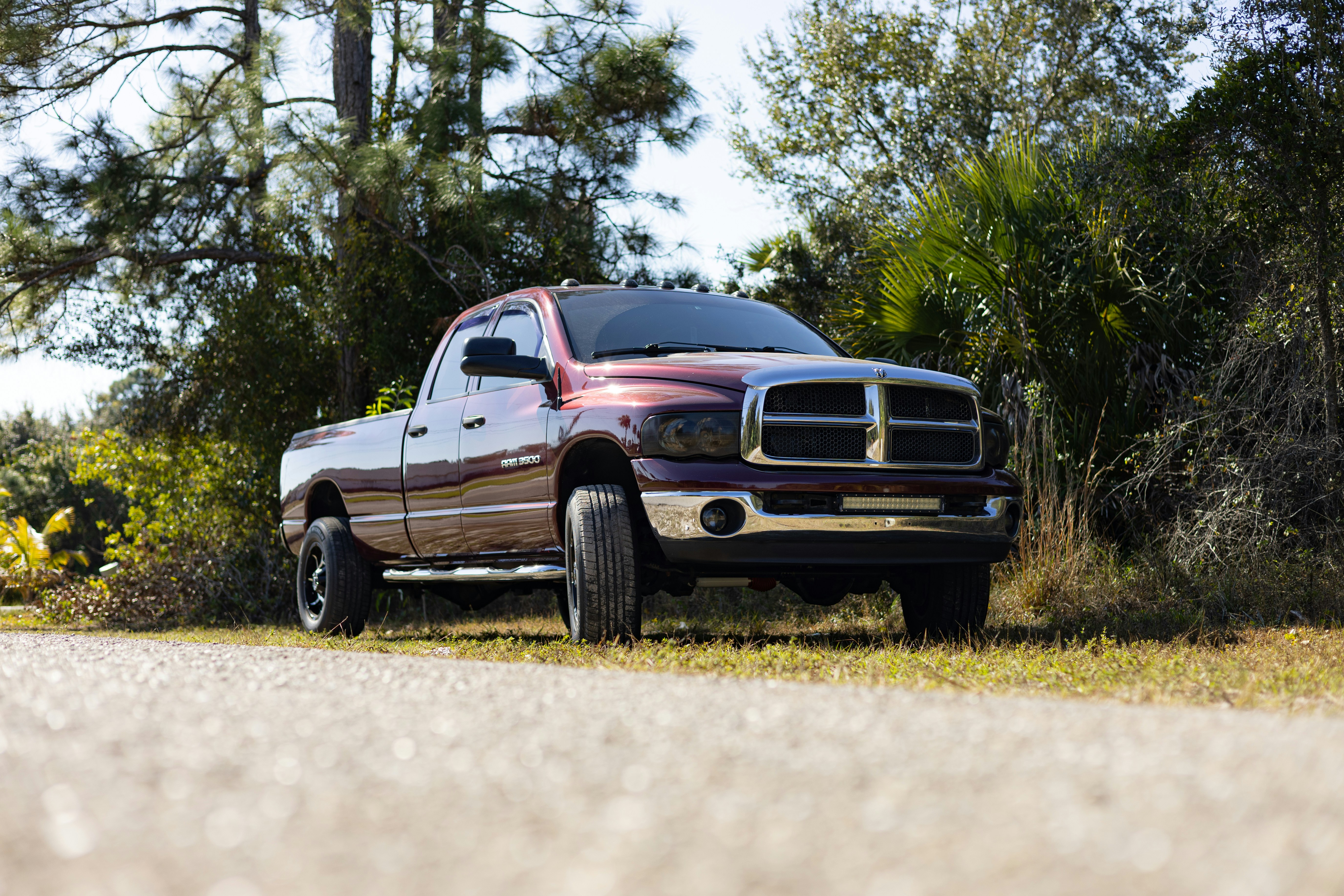 A maroon pickup truck parked on a dirt road.