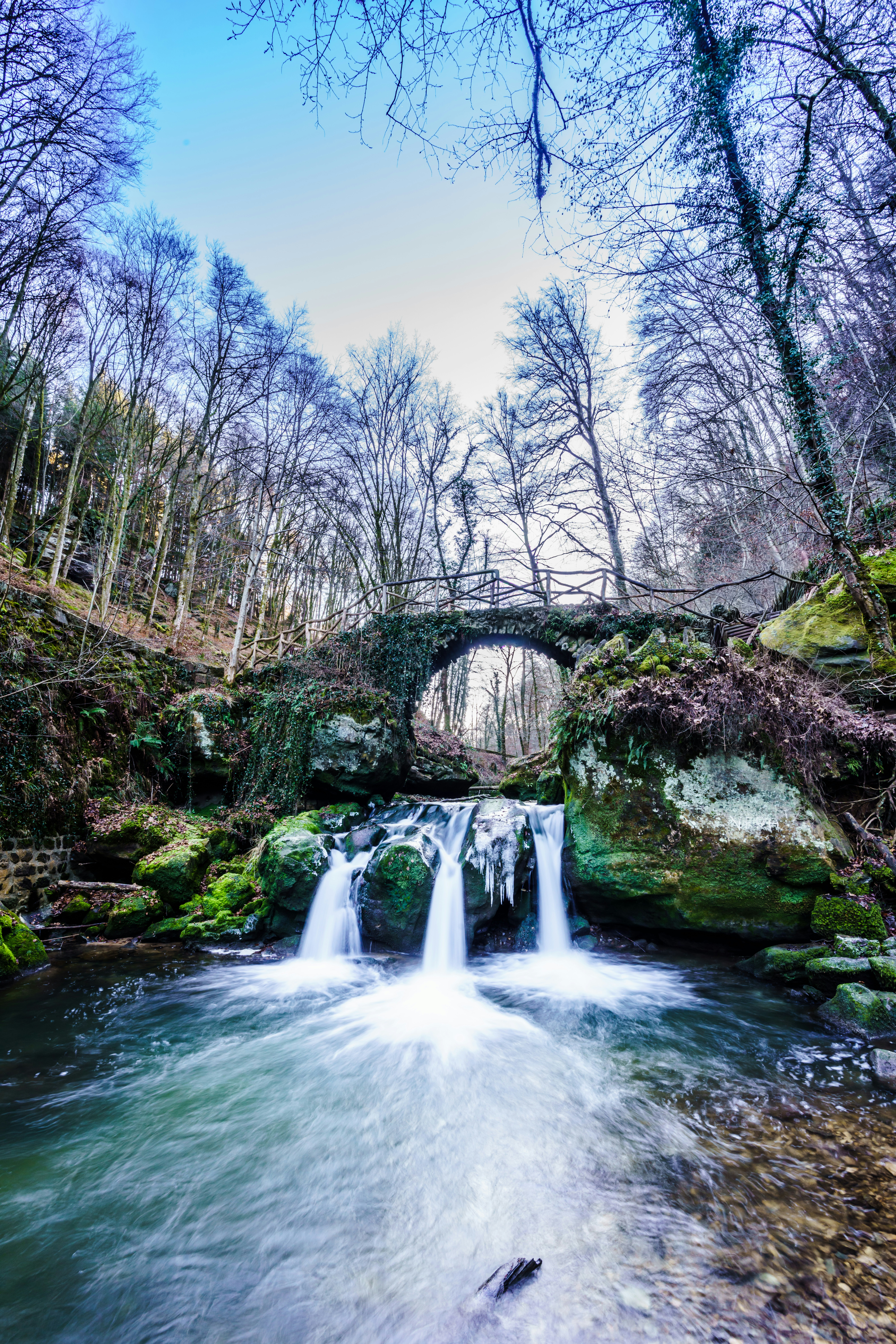 Cachoeira correndo sob uma ponte de pedra na floresta de inverno