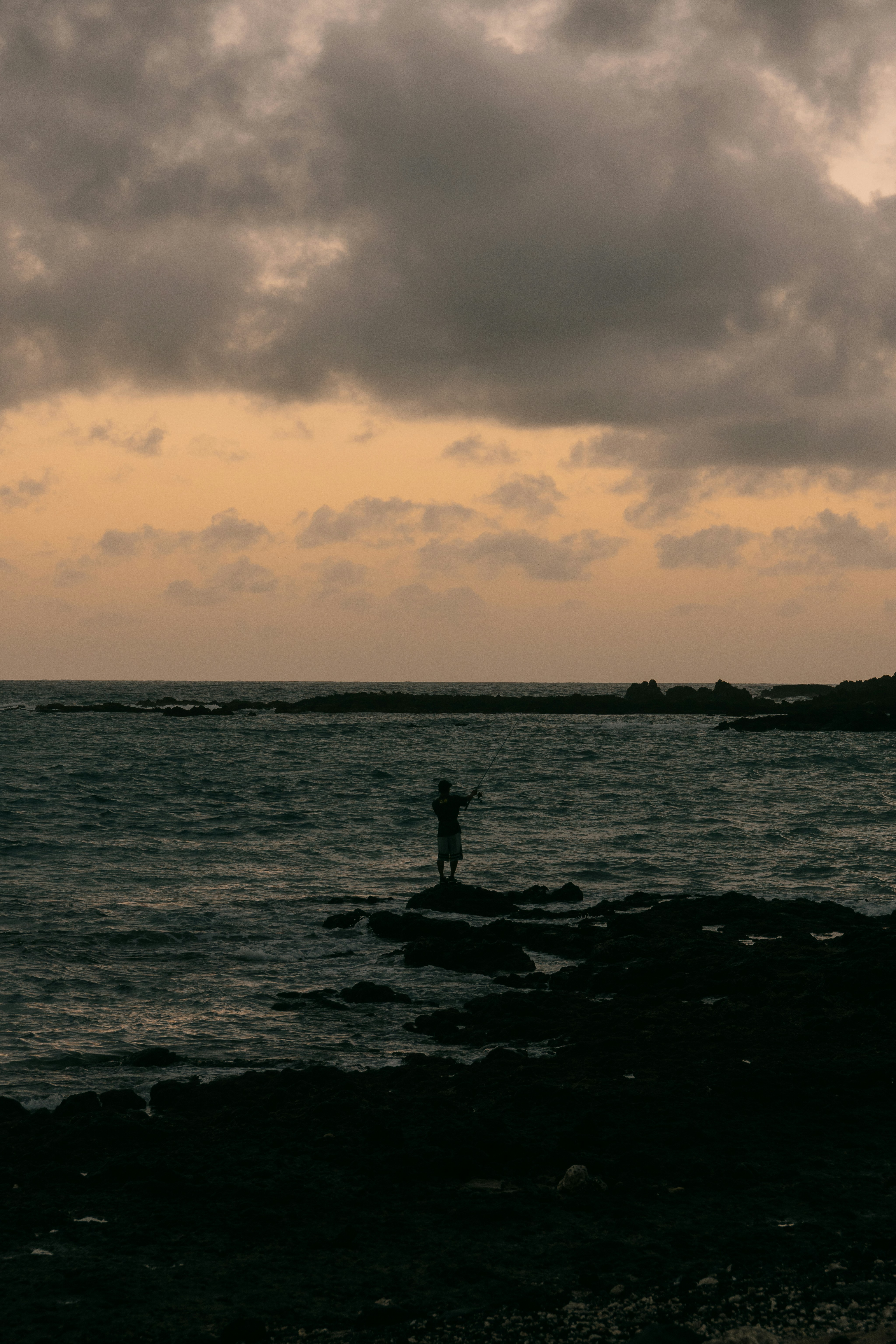 Homme pêcheant depuis une côte rocheuse au coucher du soleil