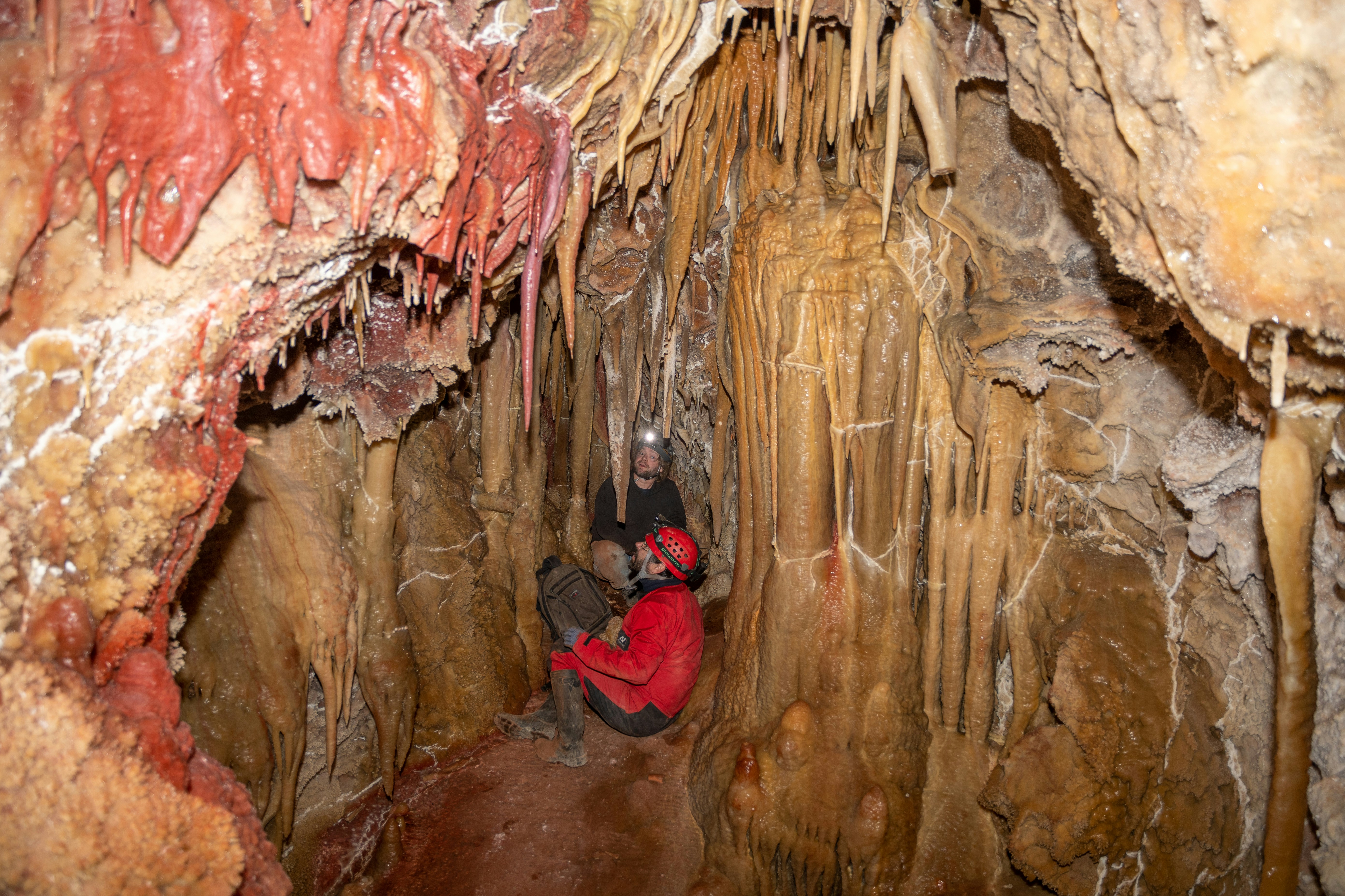 Two explorers examining cave formations with headlamps.